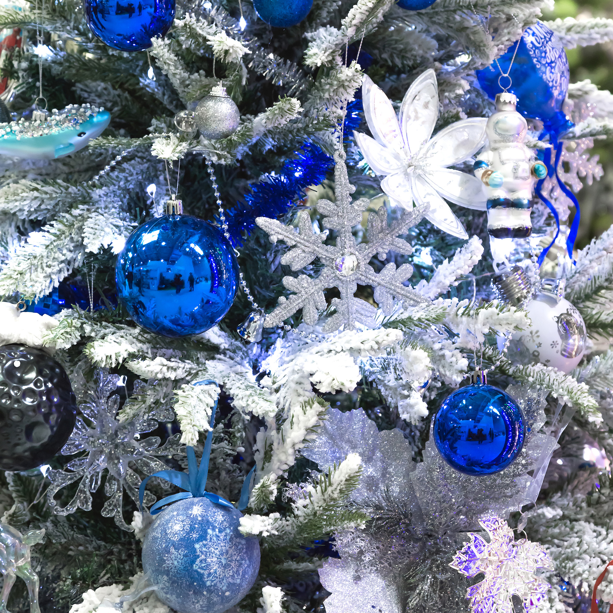 Un árbol de Navidad decorado con adornos azules y plateados, que incluyen bolas, copos de nieve y un astronauta, cubierto de nieve.