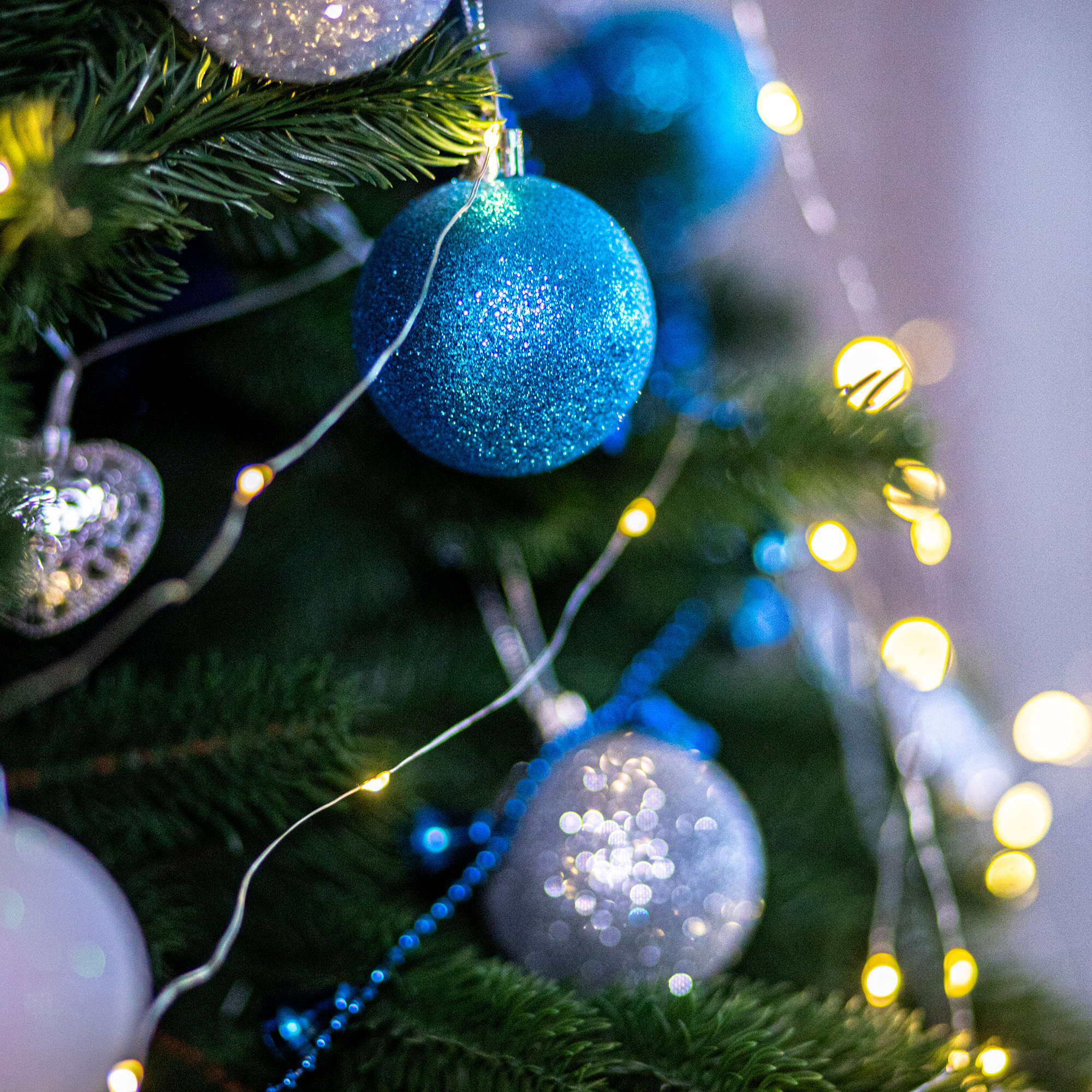 Primer plano de un árbol de Navidad con adornos azules y plateados, luces de hadas y ramas verdes, creando un ambiente festivo.