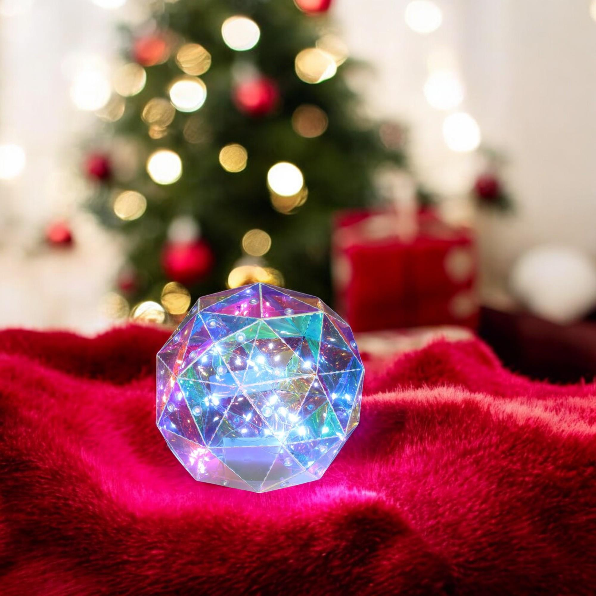 Una esfera de vidrio facetado con luces está sobre piel roja, con un árbol de Navidad borroso y regalos al fondo.
