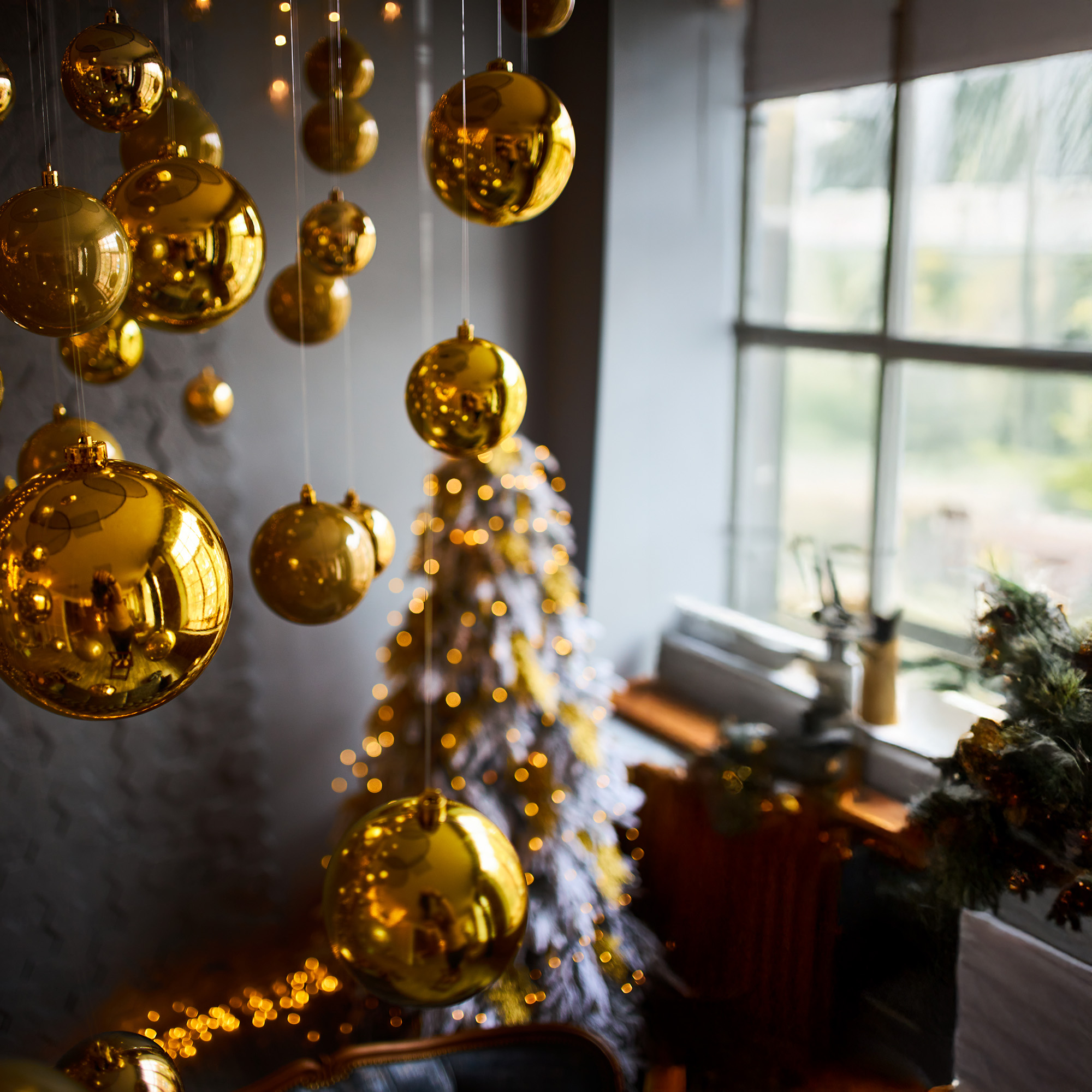 Adornos navideños dorados colgando. Un árbol y una ventana están al fondo. Iluminación cálida y festiva.