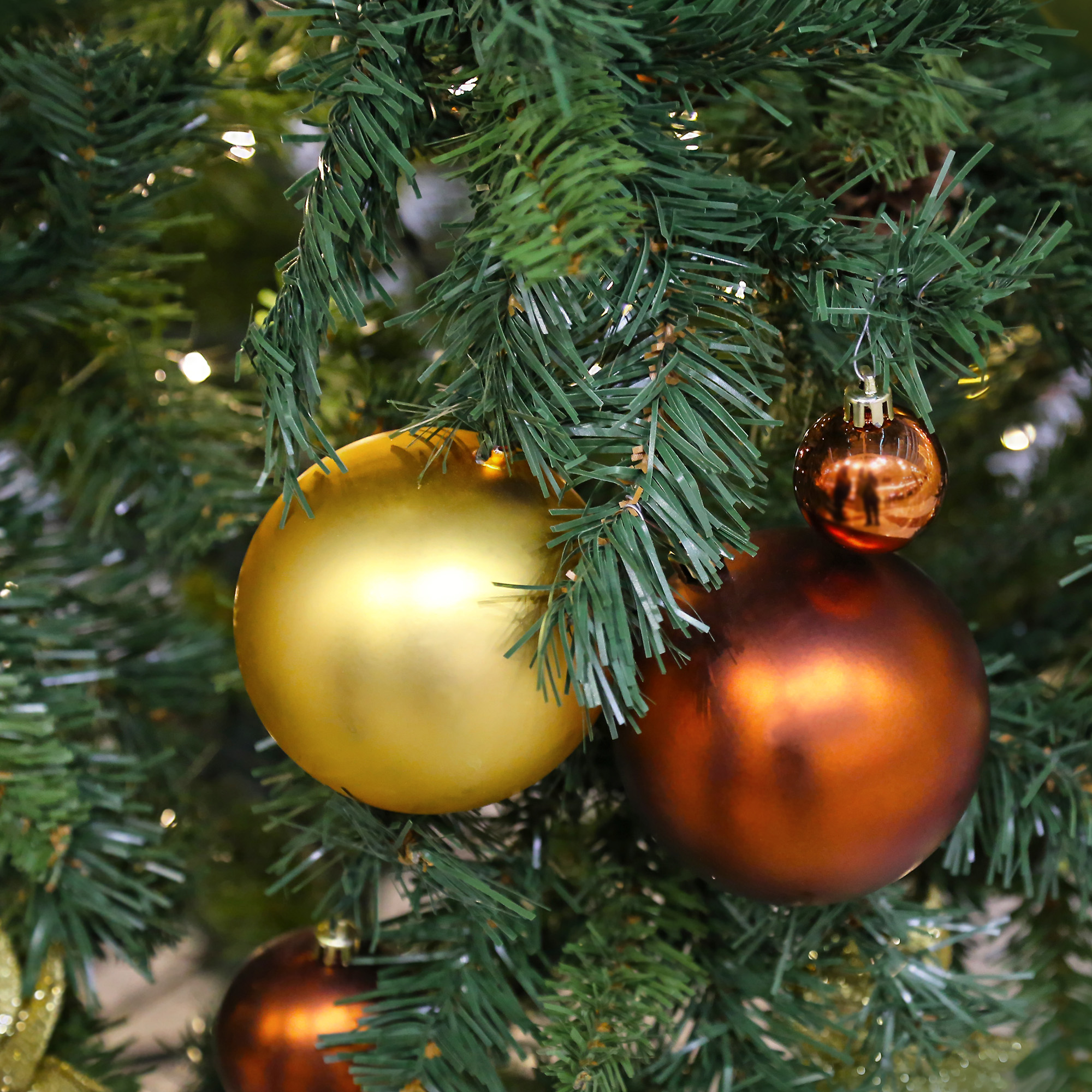 Primer plano de un árbol de Navidad con adornos dorados y cobrizos. Agujas verdes rodean las bolas.