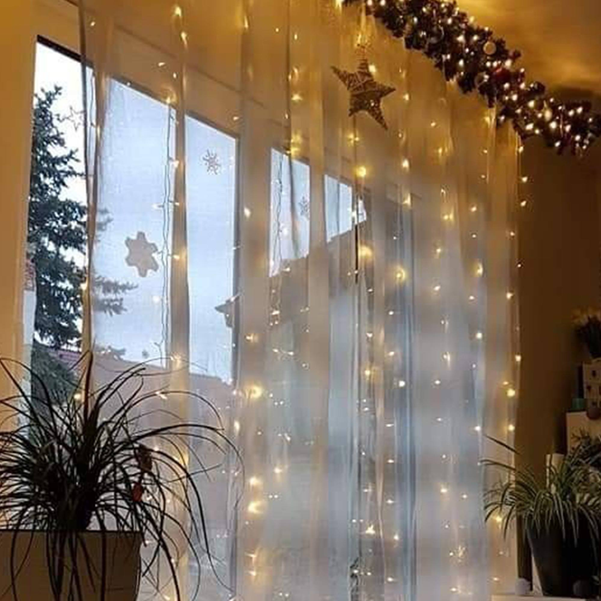Ventana con luces de hadas, decoración de estrellas y plantas. Afuera, una escena nevada.