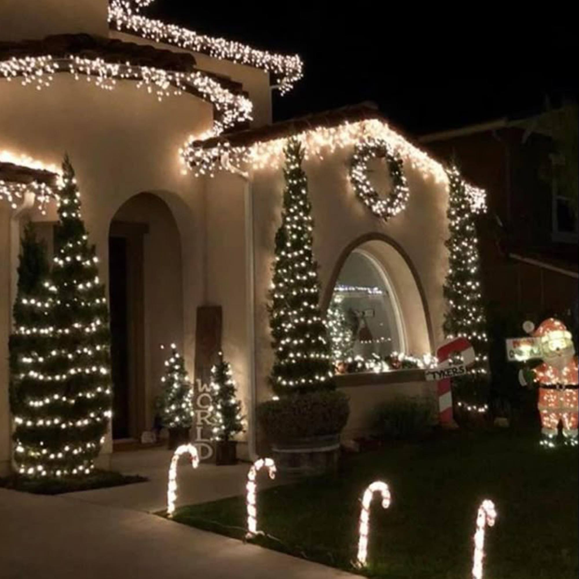 Una casa de noche, decorada con luces navideñas. Árboles iluminados, bastones de caramelo y una figura de Papá Noel.