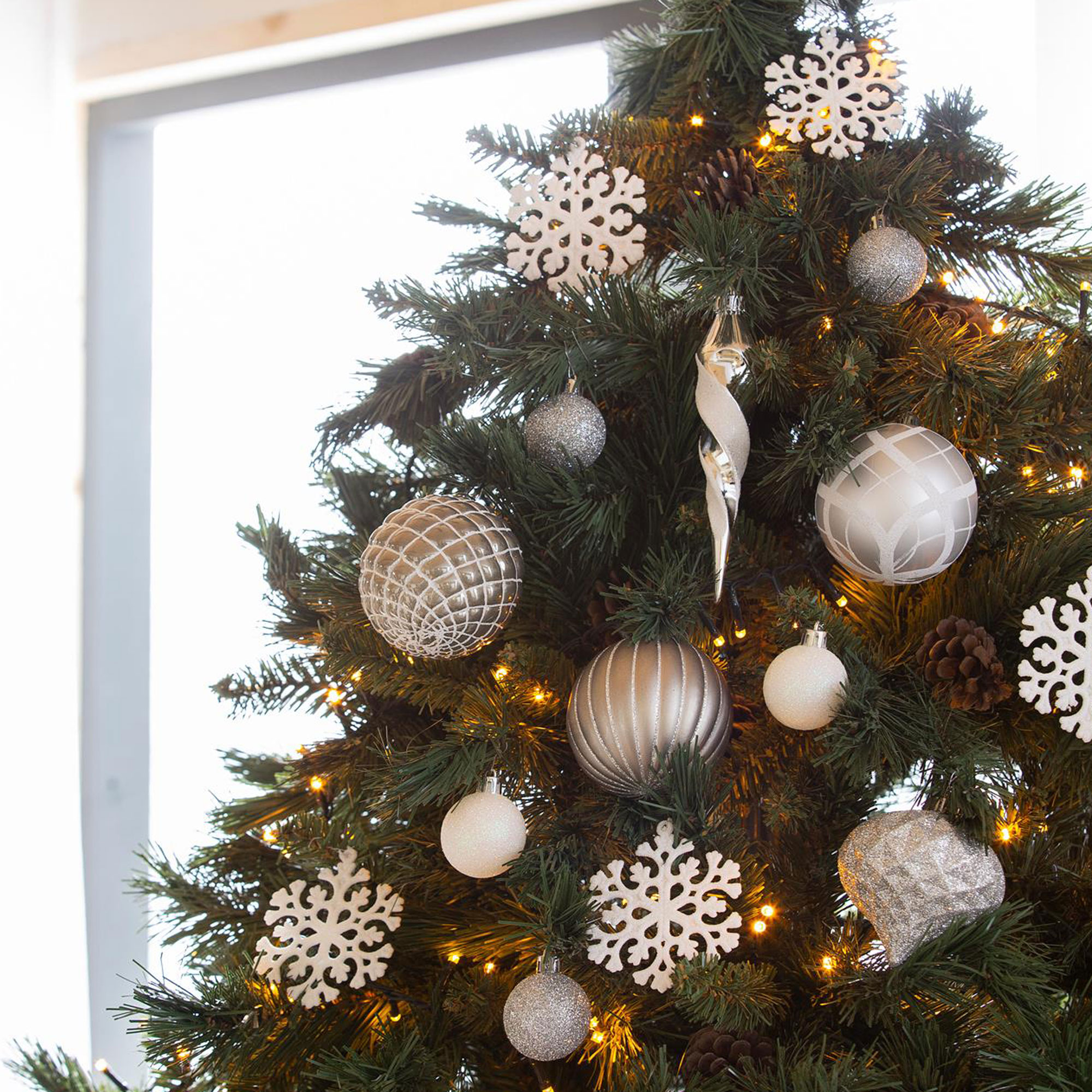 Un árbol de Navidad decorado con adornos, copos de nieve y luces. Hay una ventana en el fondo.
