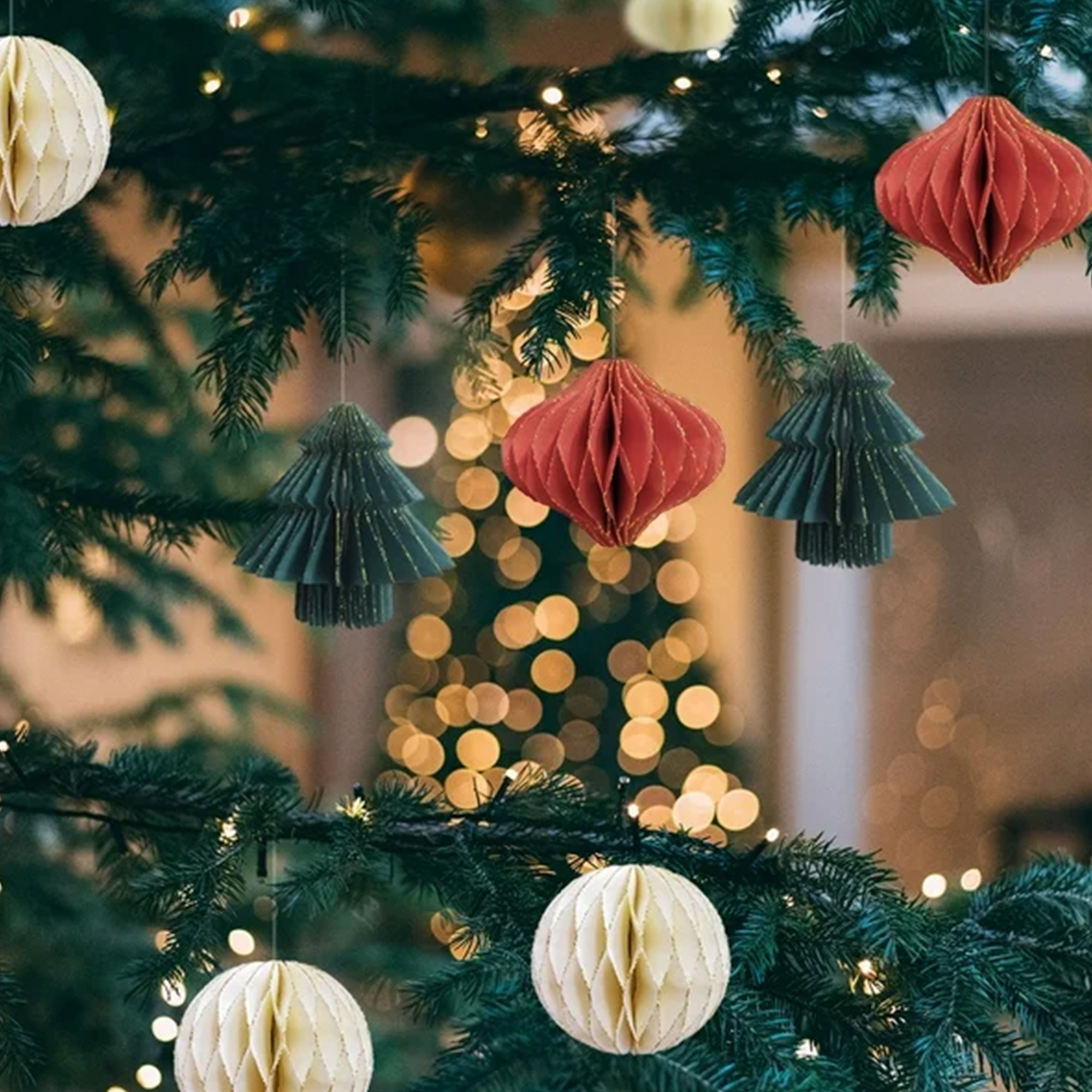 Árbol de Navidad decorado con adornos de papel colgantes, incluyendo formas de árbol rojas y verdes y bolas de panal blancas.
