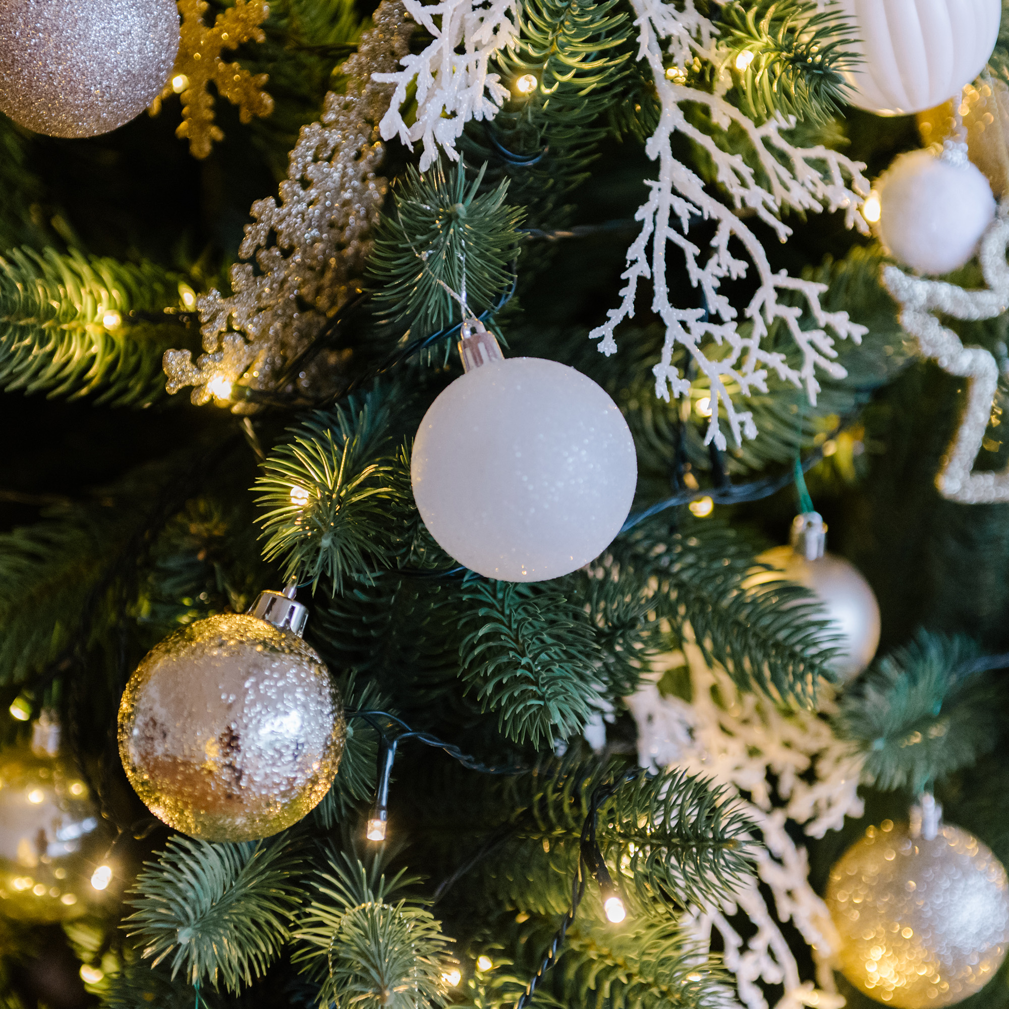 Primer plano de un árbol de Navidad decorado con adornos, luces y elementos decorativos blancos.