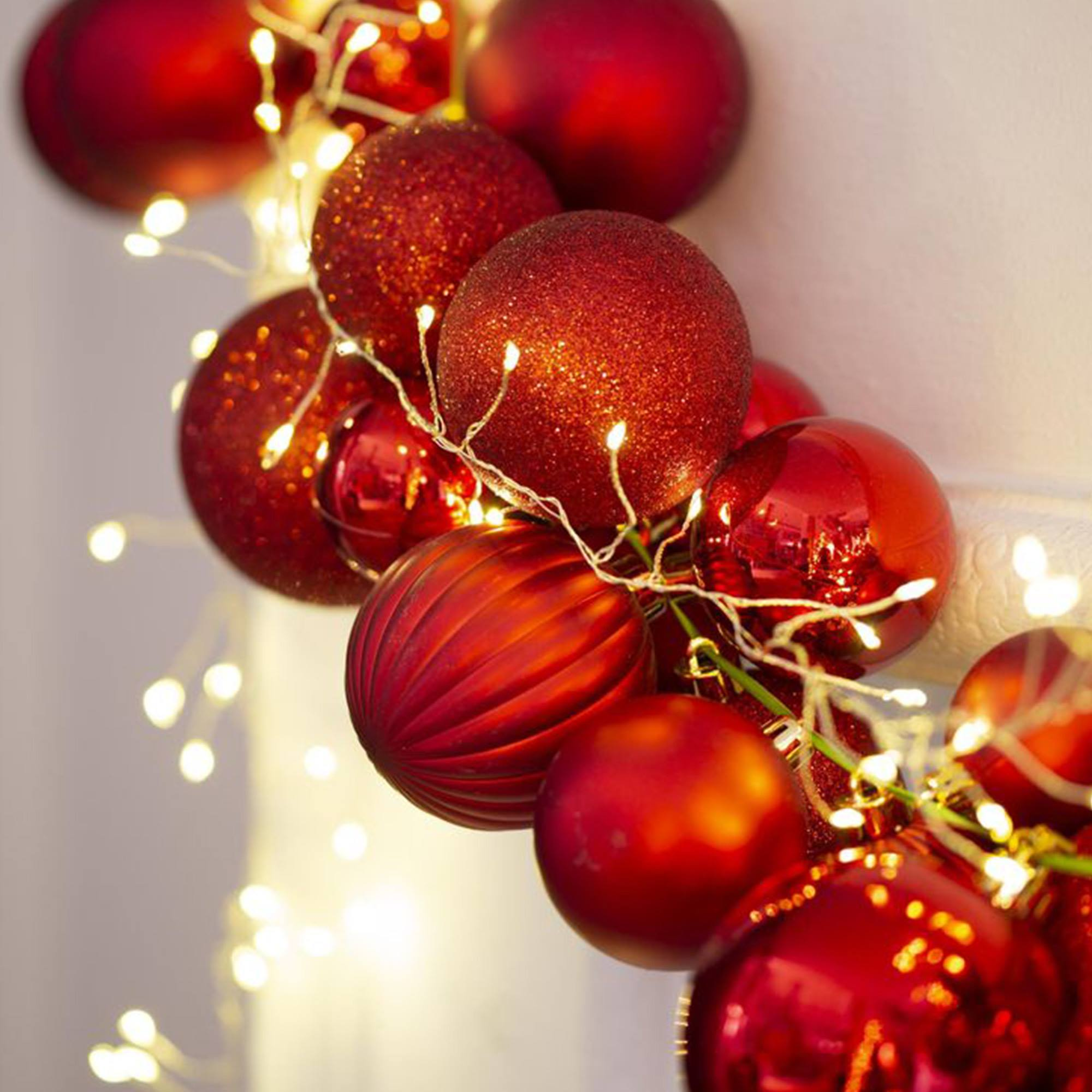 Primer plano de adornos navideños rojos con pequeñas luces blancas. Algunos adornos son brillantes, otros lisos.