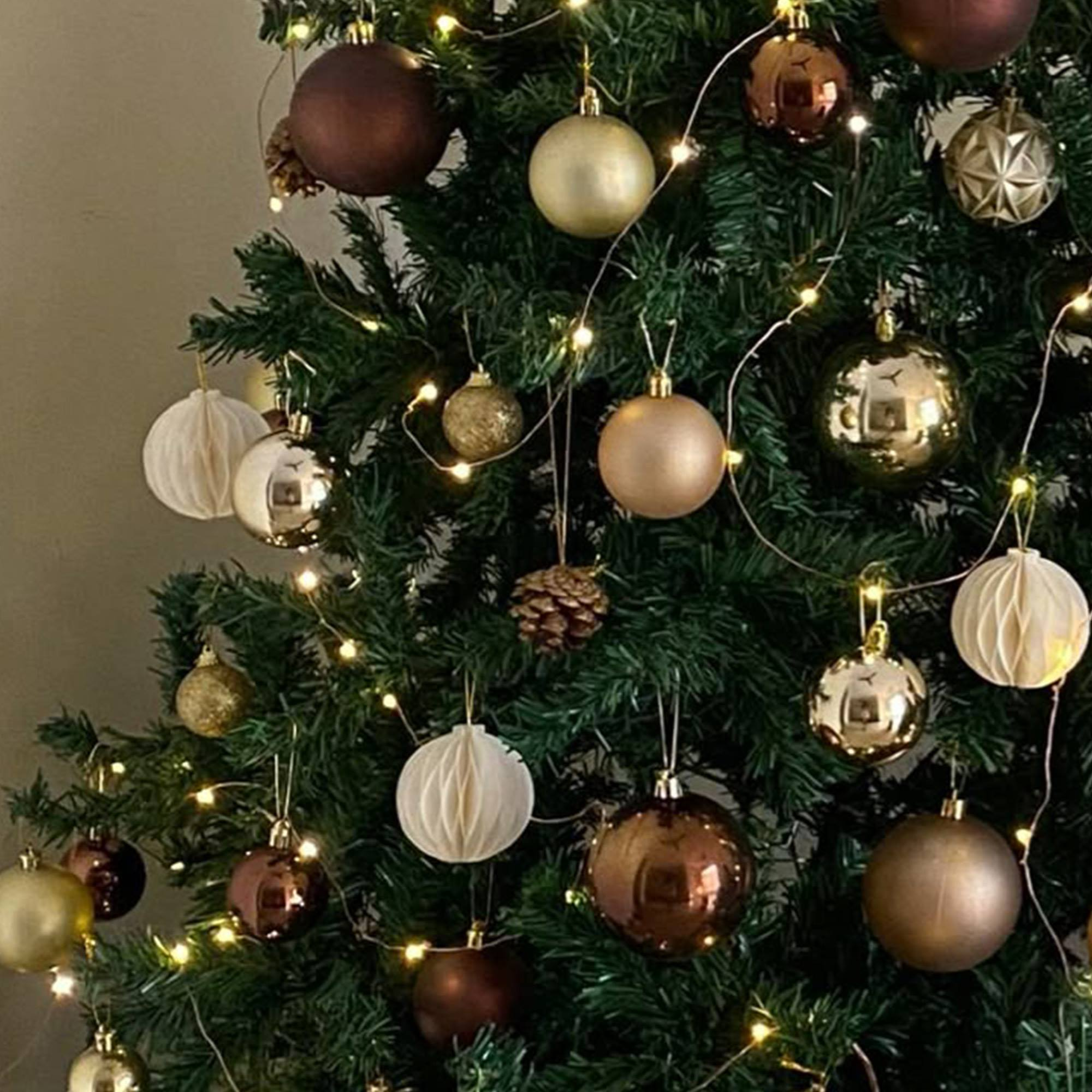 Árbol de Navidad decorado con adornos dorados y marrones, con pequeñas luces. También hay una piña.