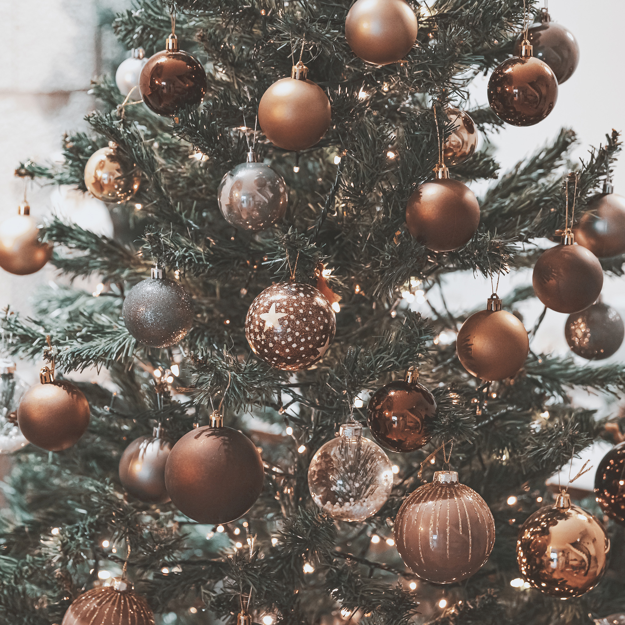 Un árbol de Navidad decorado con adornos marrones, dorados y plateados. Pequeñas luces parpadean entre las ramas. El fondo está borroso.