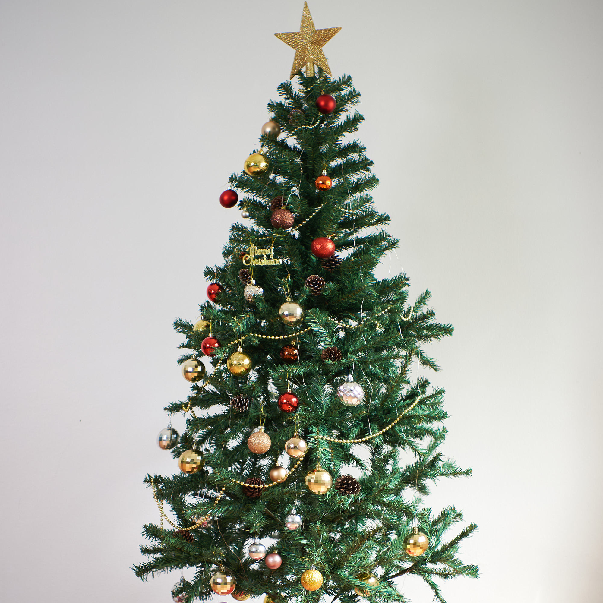 Árbol de Navidad con adornos, estrella dorada arriba, bolas rojas y doradas, piñas y un letrero que dice Feliz Navidad.