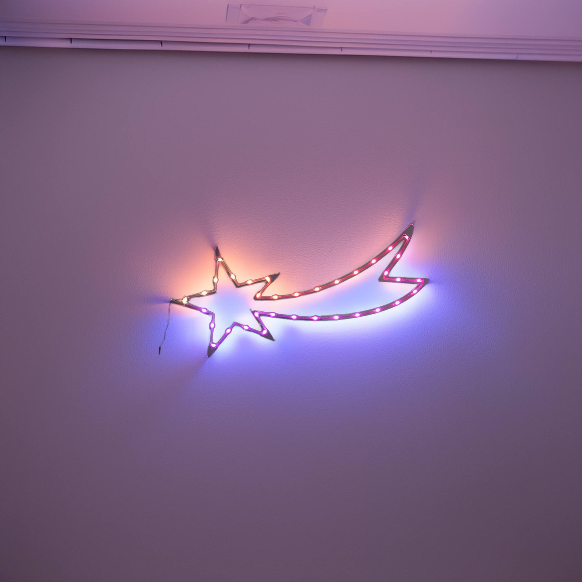 Luminaria en forma de estrella en una pared morada. Brilla con luz naranja y azul. El fondo es una pared lisa.