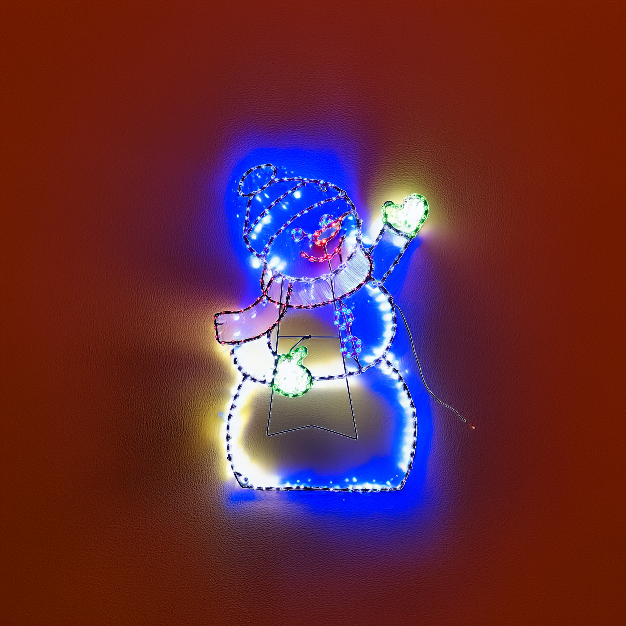 Decoración navideña de muñeco de nieve. Tiene sombrero y bufanda azules. El fondo es marrón.