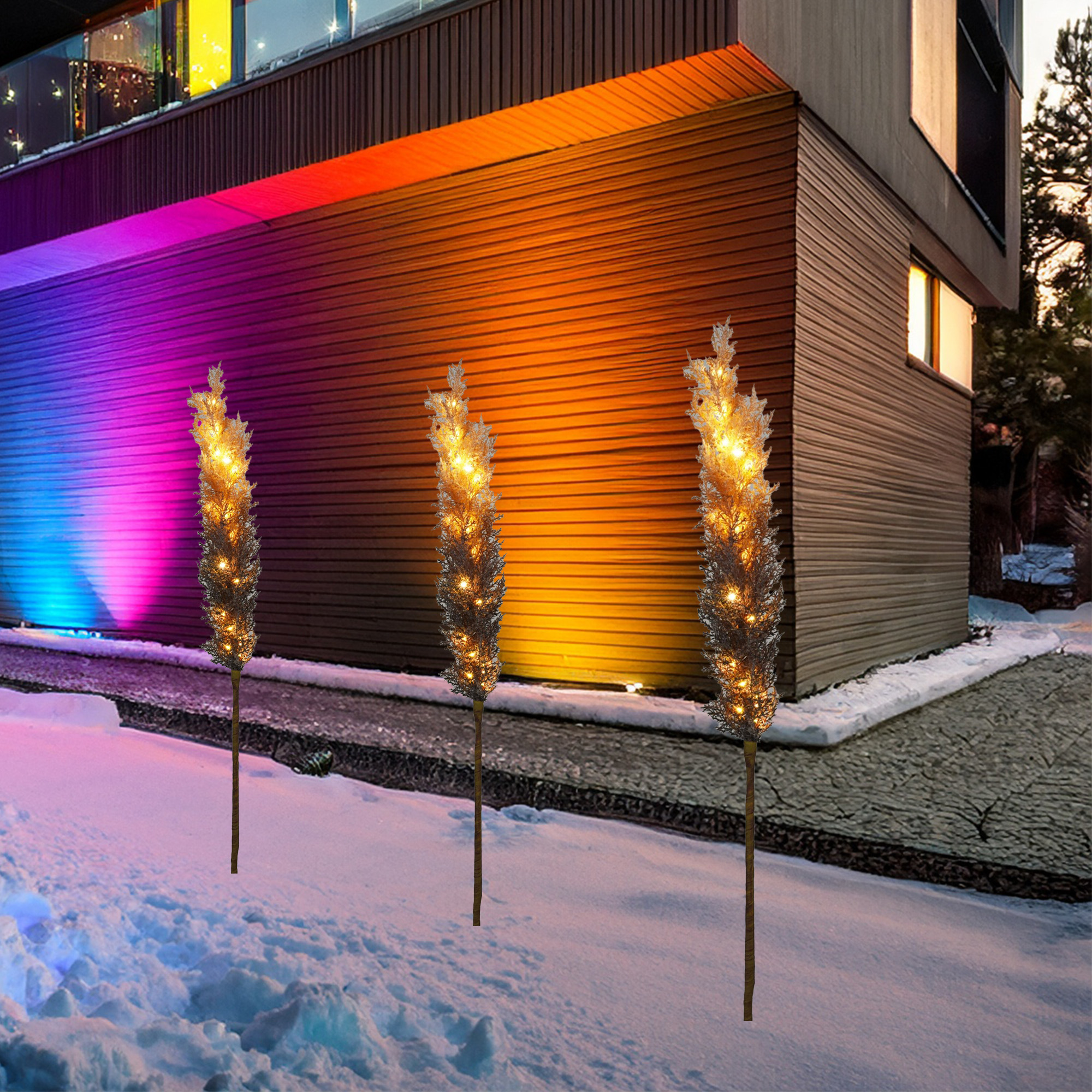 Tres plantas decorativas iluminadas en la nieve. Edificio con luces cambiantes en el fondo.
