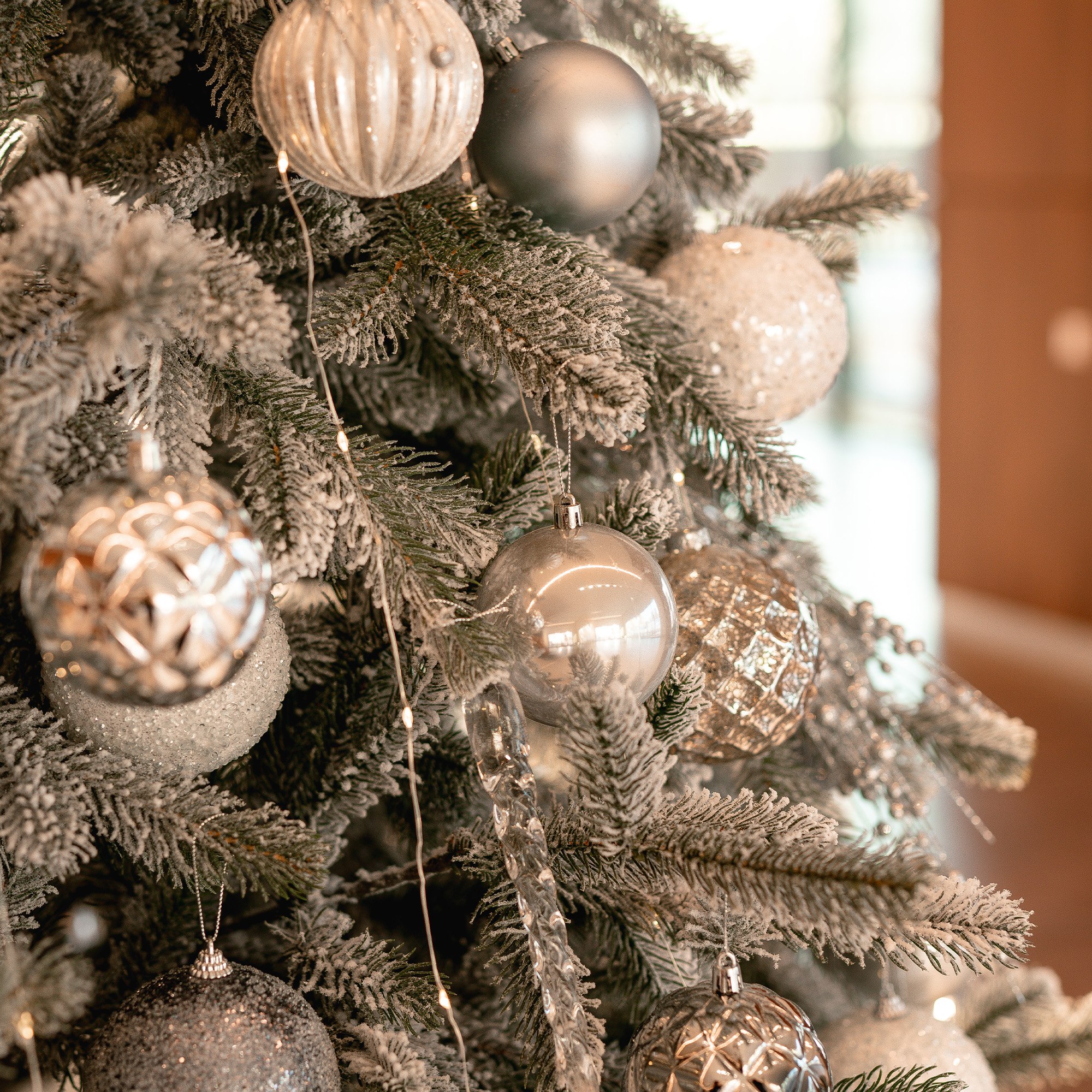 Un árbol de Navidad decorado con adornos plateados y blancos. Ramas heladas y luces suaves crean una escena festiva.