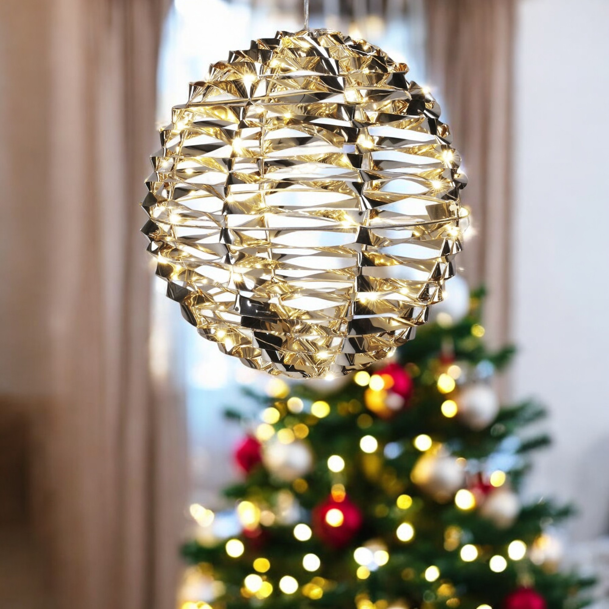 Una esfera decorativa dorada cuelga sobre un árbol de Navidad con adornos y luces.