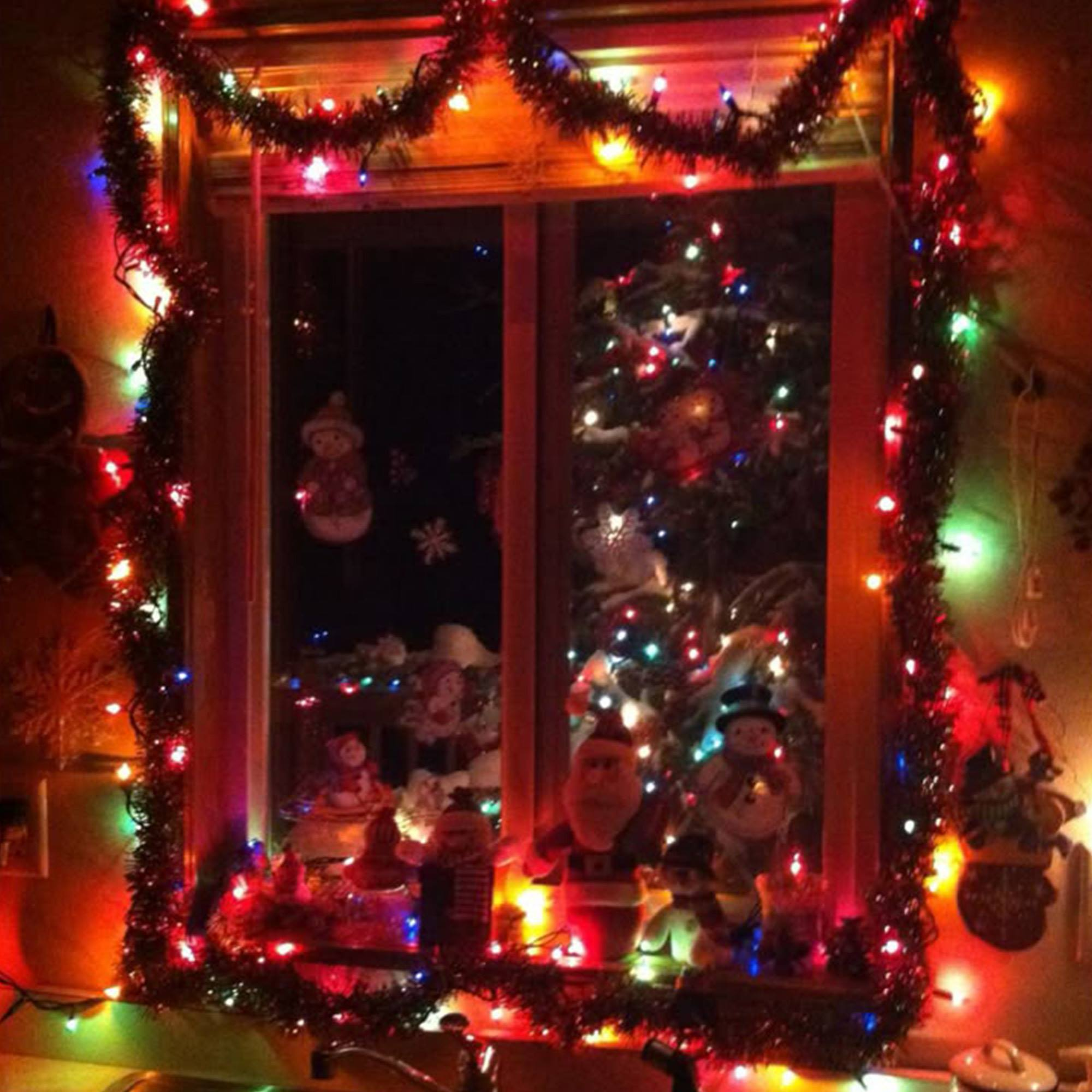 Escena navideña en una ventana con luces, adornos y un árbol. Decoraciones festivas y fondo oscuro.