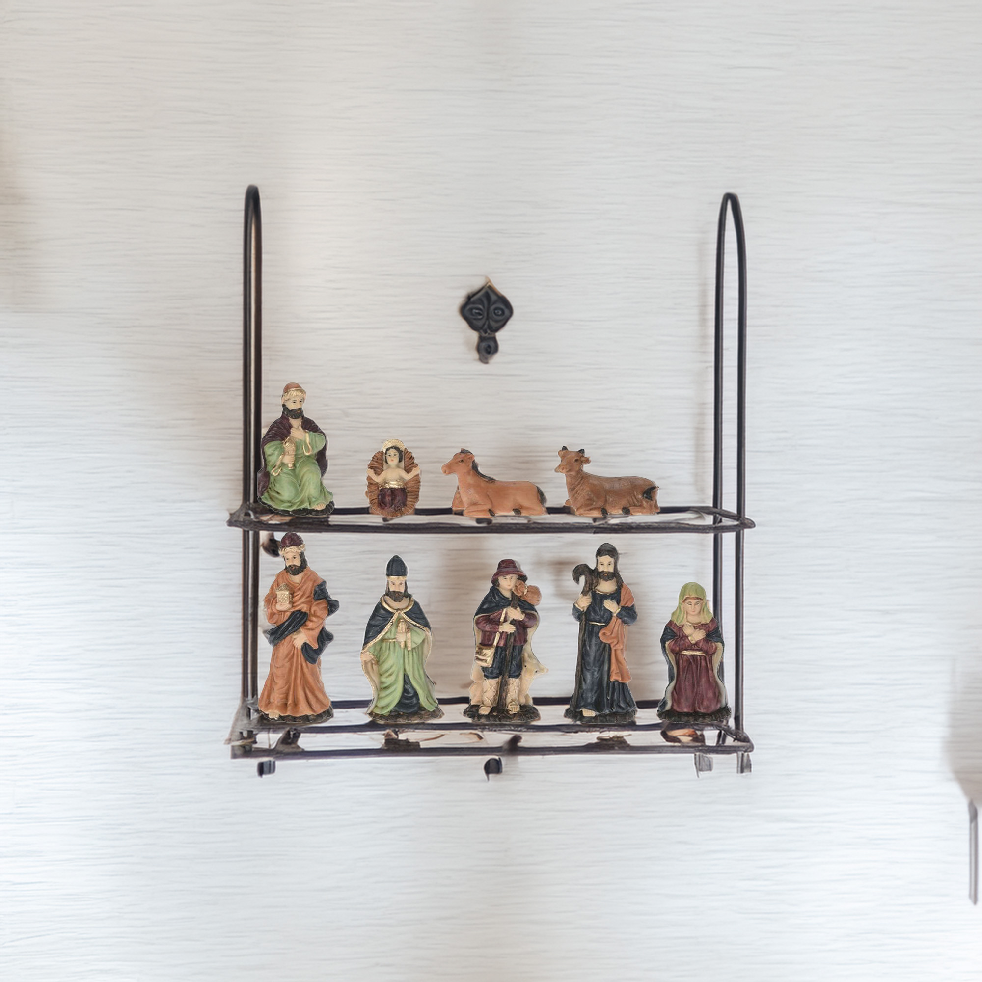 Una estantería con un belén. Incluye figuras de personas, animales y un bebé en un pesebre, todo sobre una pared blanca.