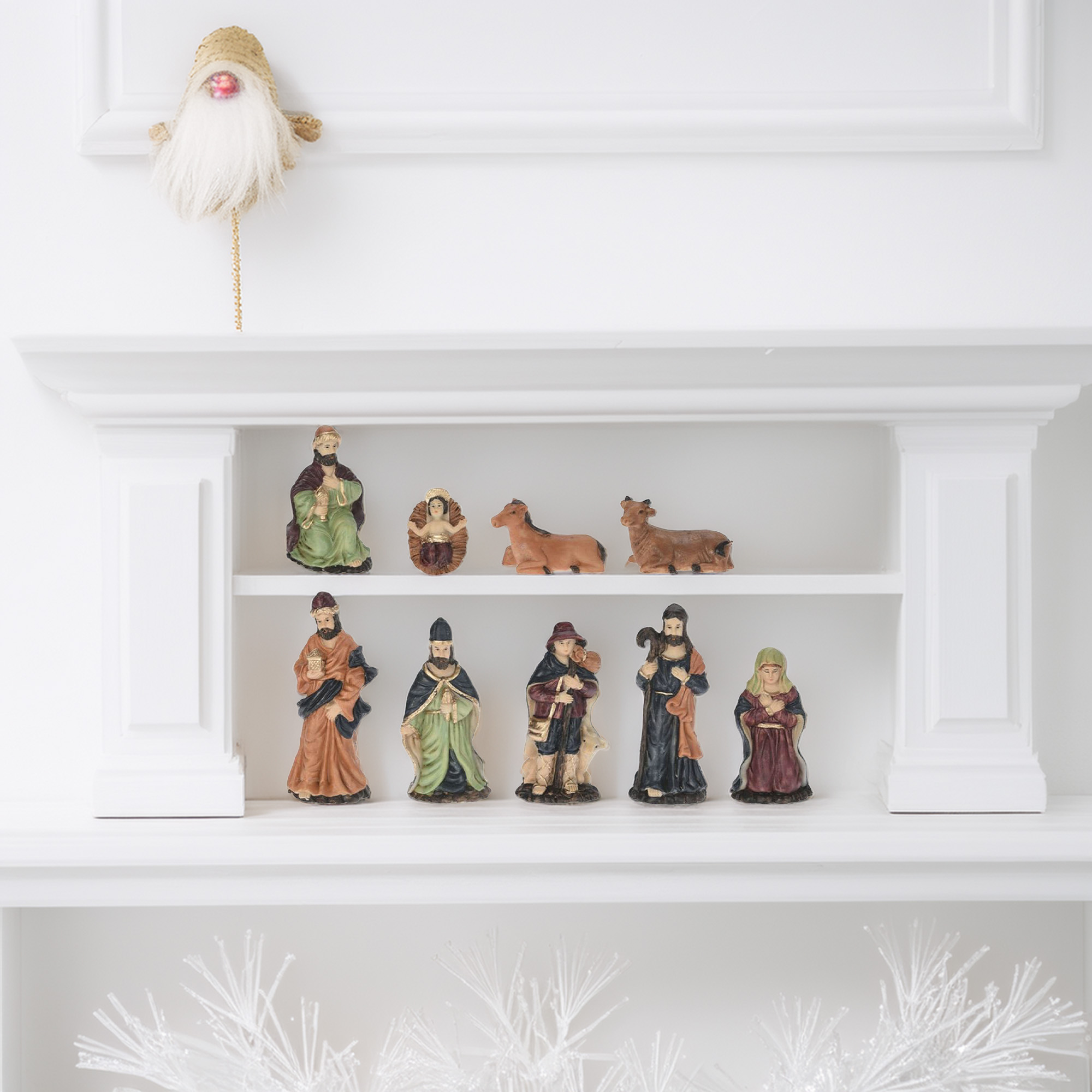 Un estante blanco exhibe una escena de la natividad. Una decoración de gnomo cuelga arriba. El primer plano presenta una decoración blanca y puntiaguda.