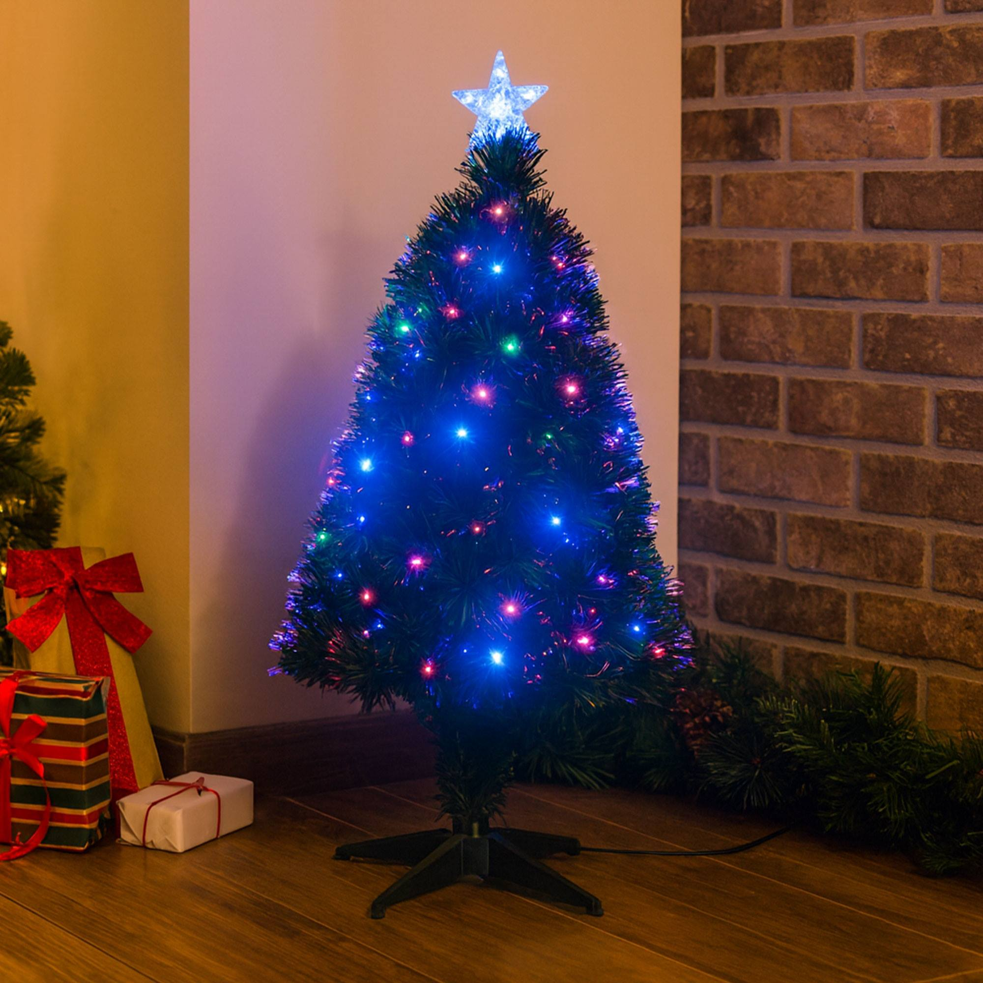 Un pequeño árbol de Navidad con luces, estrella en la parte superior. Regalos y pared de ladrillo al fondo.