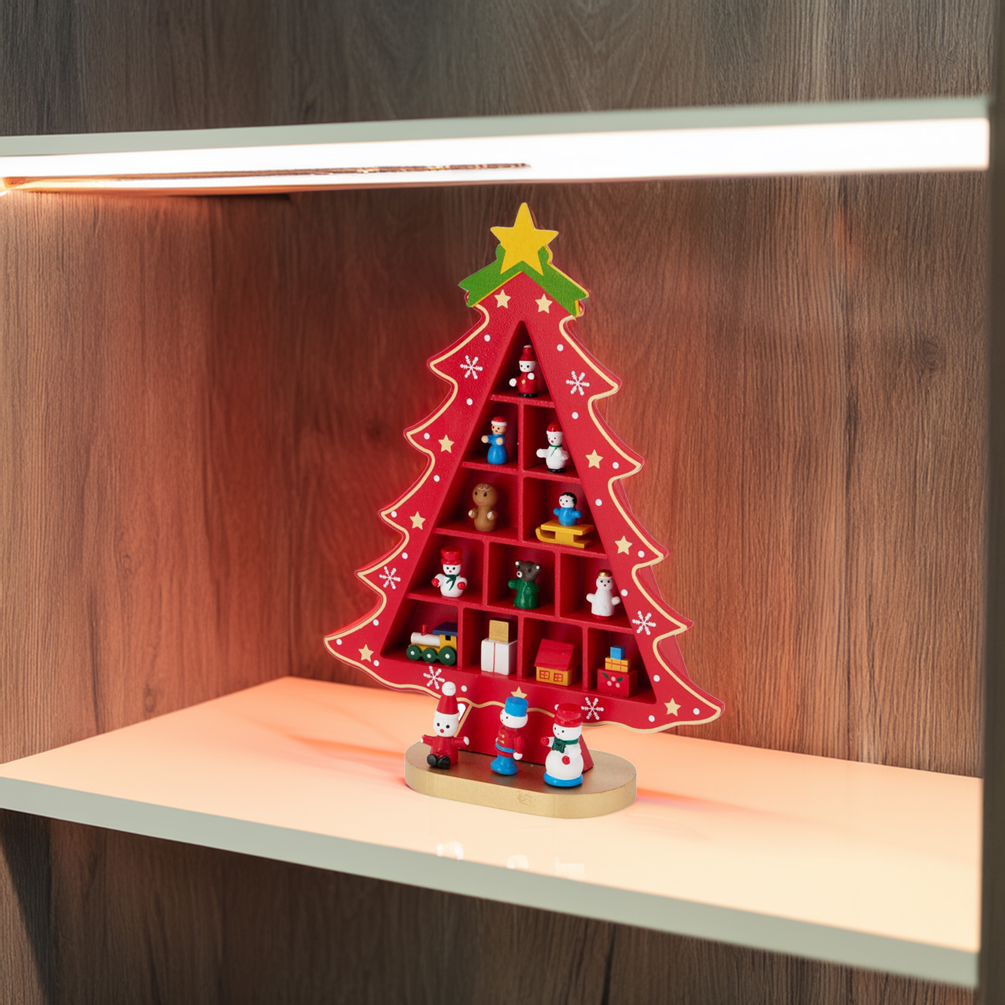 Una estantería roja en forma de árbol de Navidad con pequeñas figuras. Está sobre una estantería blanca frente a una pared de madera.