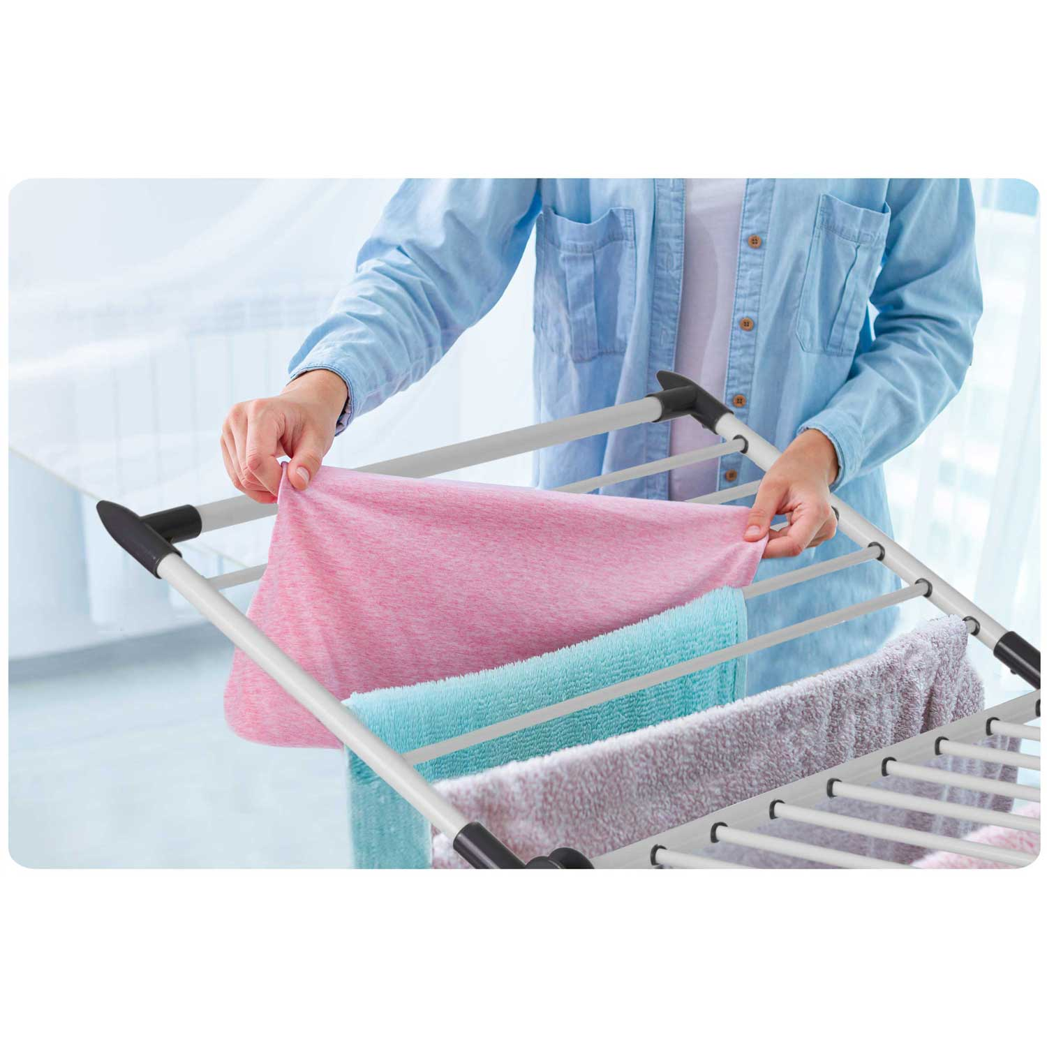 Osoba wiesza różowy ręcznik na suszarce do ubrań. Inne ręczniki w różnych kolorach są już powieszone.