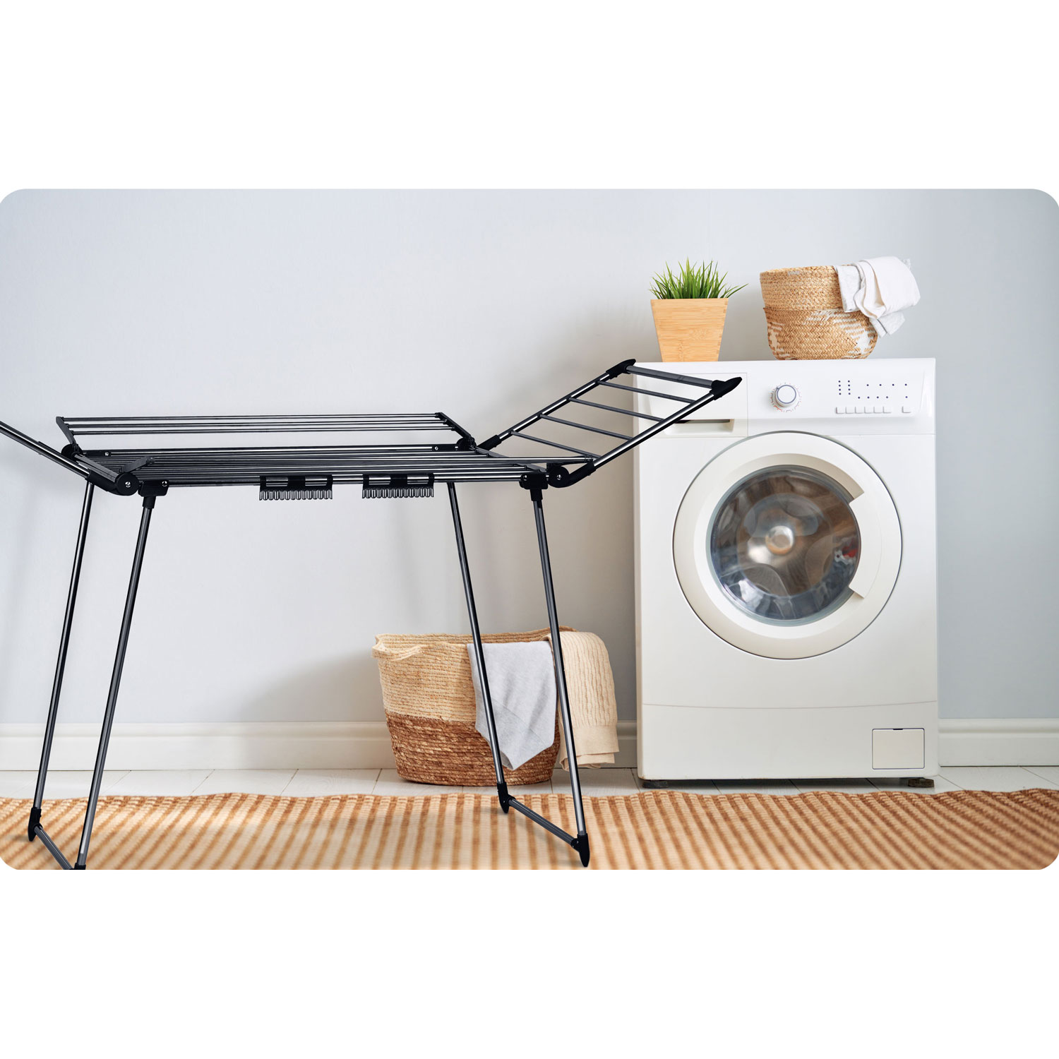 Pralnia z pralką, suszarką i dwoma koszami. Jeden kosz zawiera rośliny, drugi ręczniki.