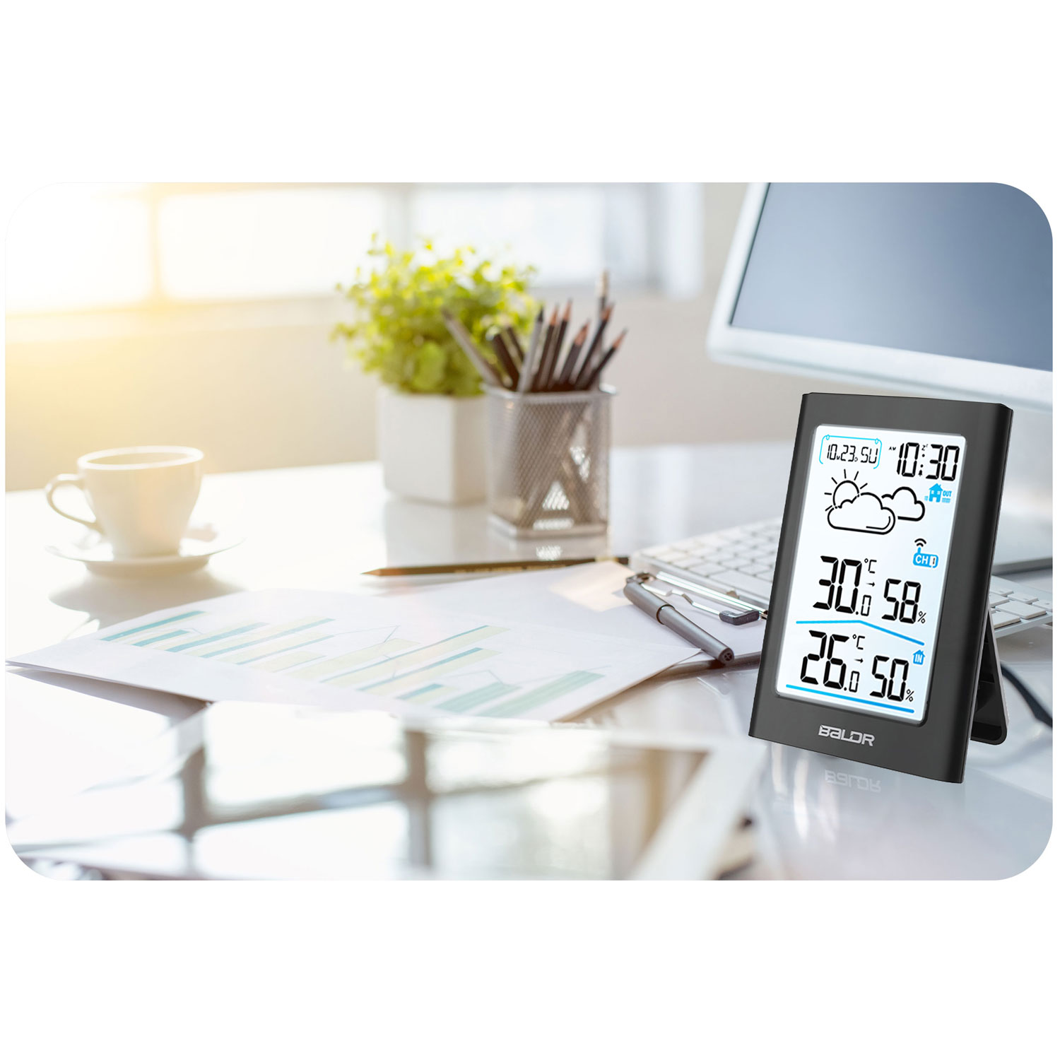 Scena biurowa: stacja pogodowa, komputer, filiżanka, roślina, długopis i dokumenty. Stacja pokazuje temperaturę i wilgotność, jest 10:30.