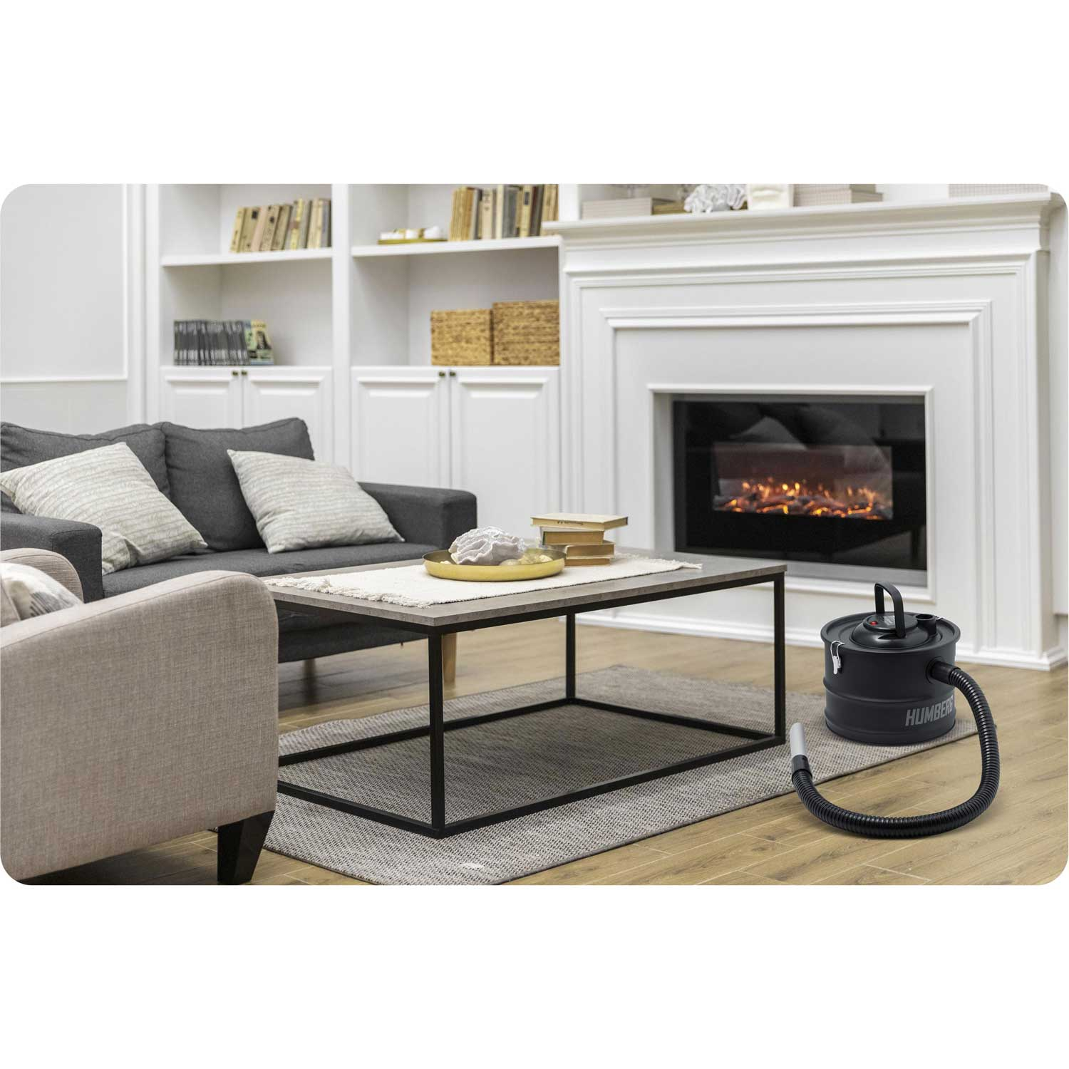 Salon z szarą sofą, stolikiem kawowym, kominkiem i odkurzaczem na podłodze. Regały z książkami w tle.