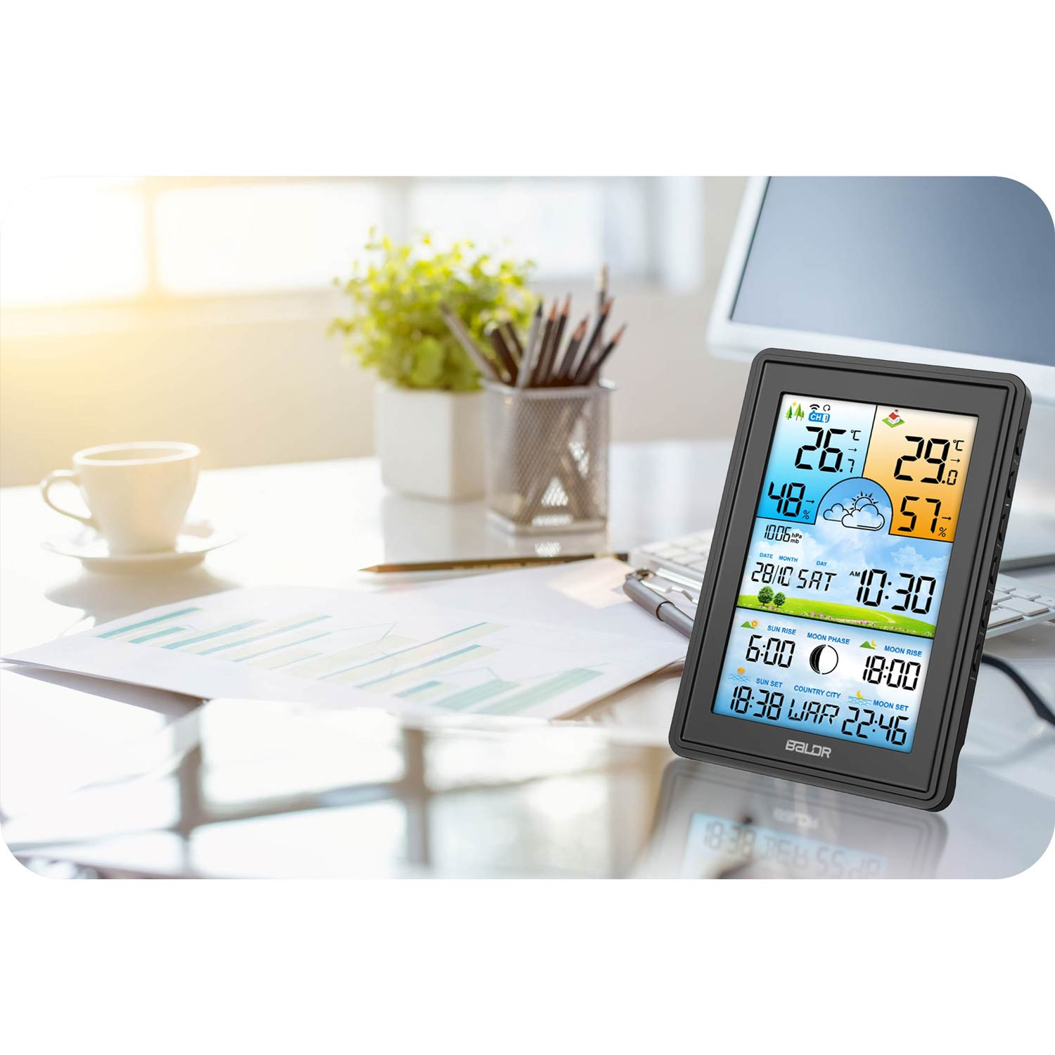 Cyfrowa stacja pogodowa wyświetla temperaturę, wilgotność i czas. Na biurku filiżanka, roślina i wykres.