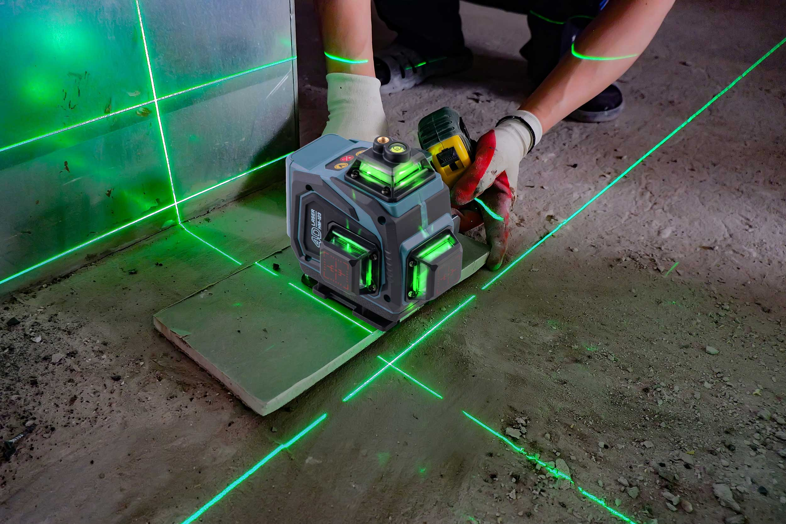 Osoba używa poziomicy laserowej na budowie. Zielone linie lasera się wyświetlają. Urządzenie jest na szarej płytce.