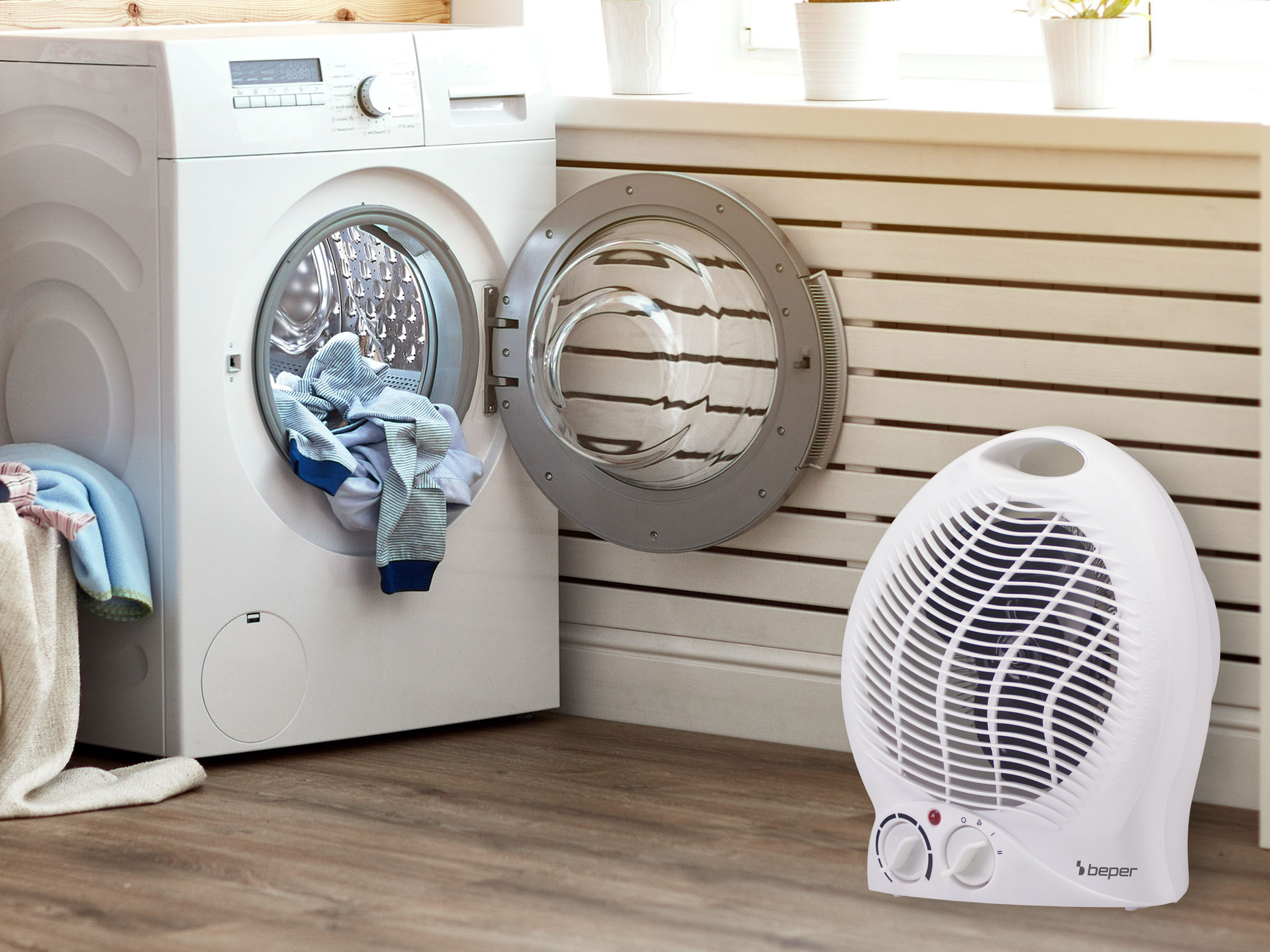 Una lavatrice con la porta aperta, vestiti all'interno e un ventilatore bianco a destra.