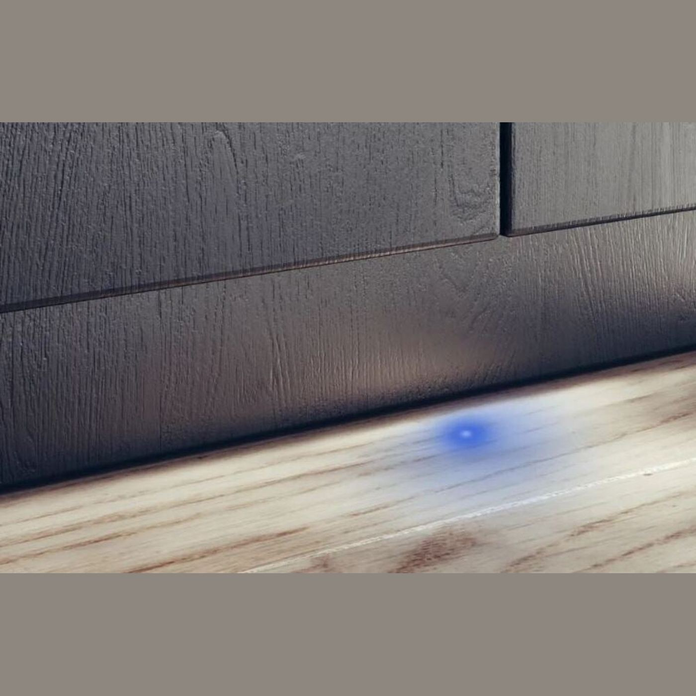 Houten kast tegen houten vloer. Een blauw licht op de vloer. De kast is donkergrijs.
