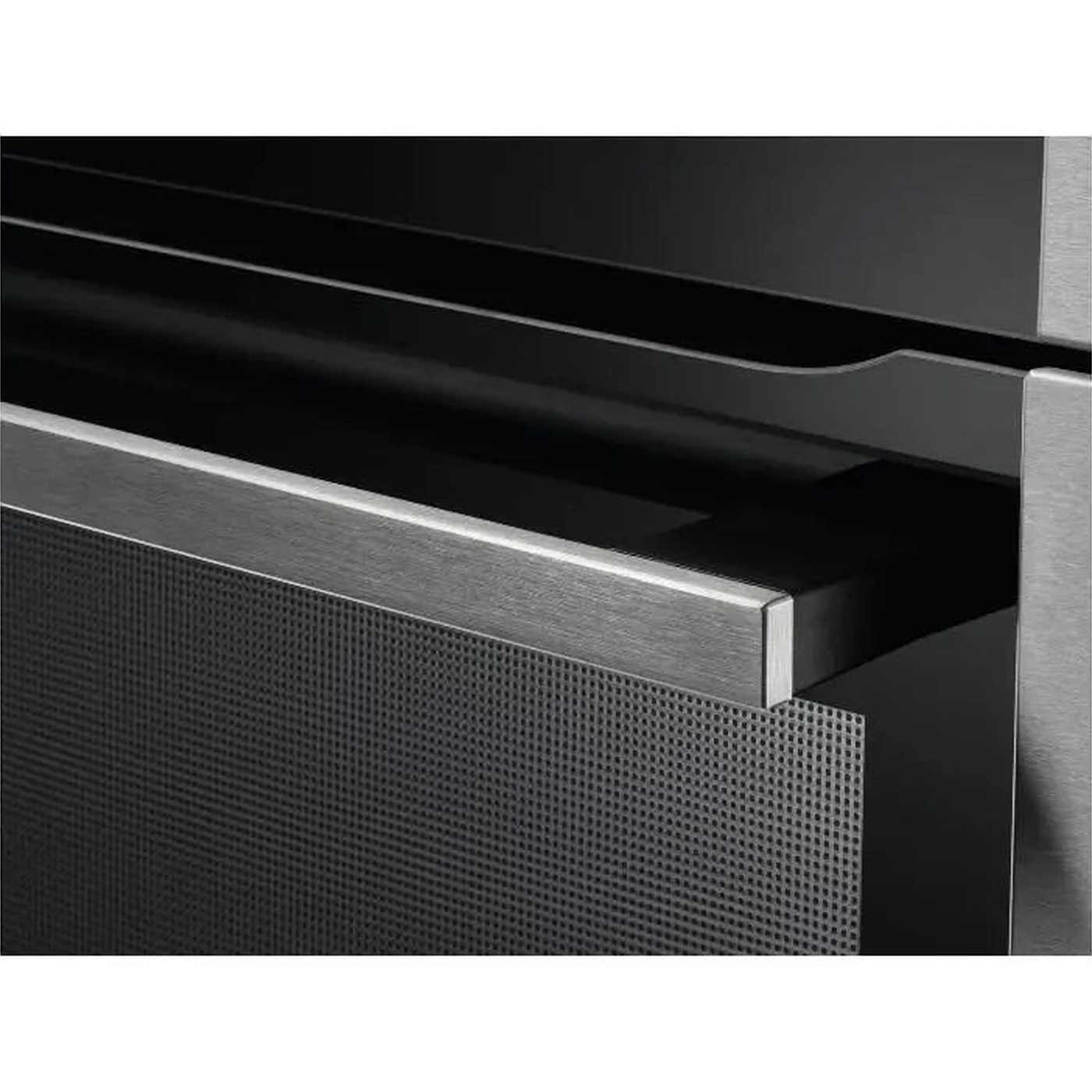 Close-up of a dark gray cabinet drawer. The drawer has a perforated front and a metallic handle. The background is dark.