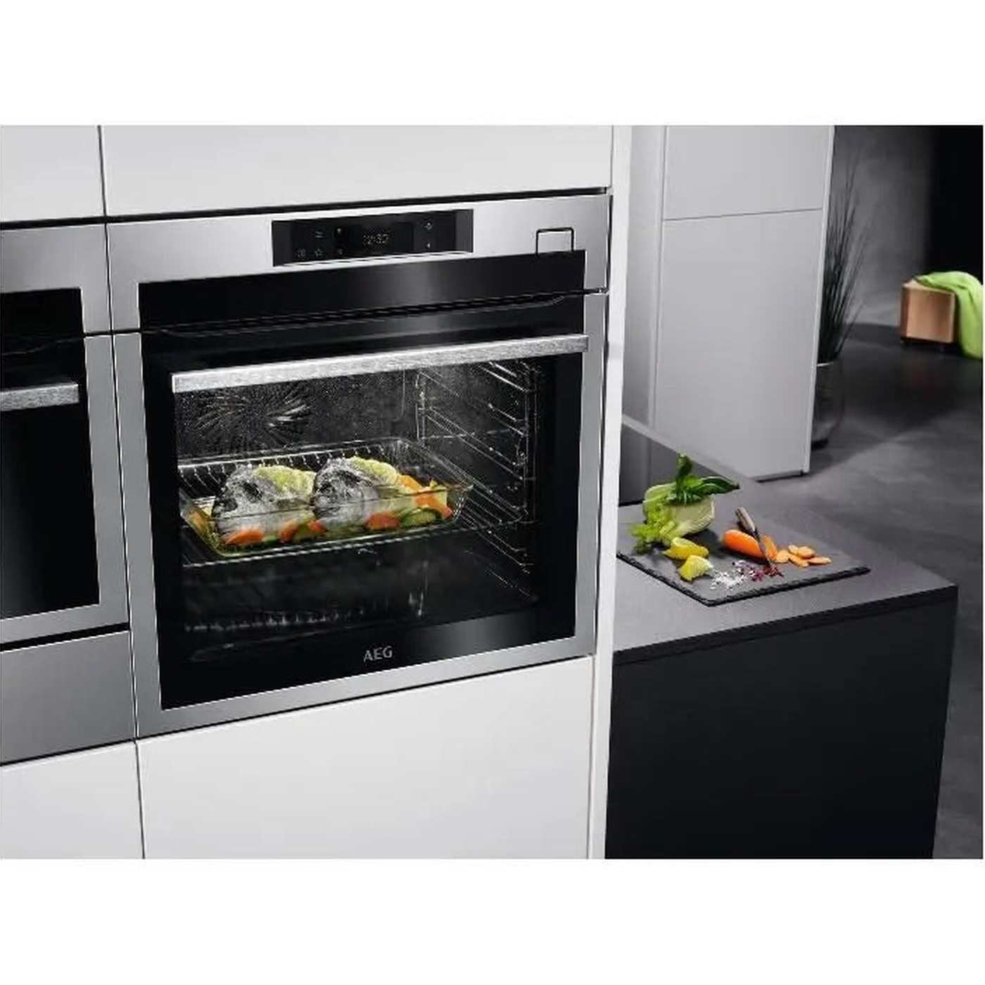 An oven with food inside. Vegetables are on a cutting board. The oven door has the AEG logo.