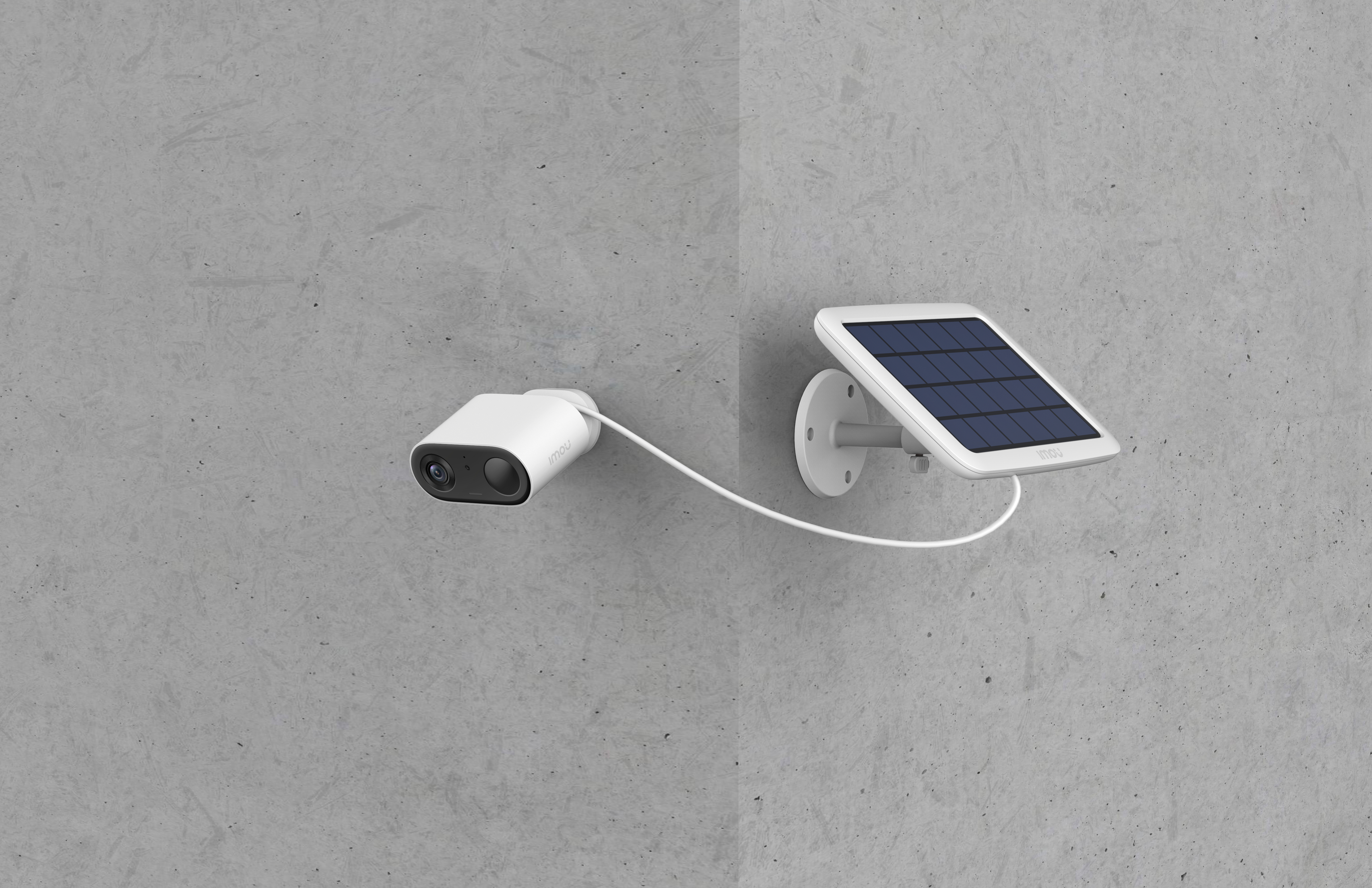 Una telecamera di sicurezza bianca e un pannello solare sono montati su un muro di cemento grigio, collegati da un cavo bianco.