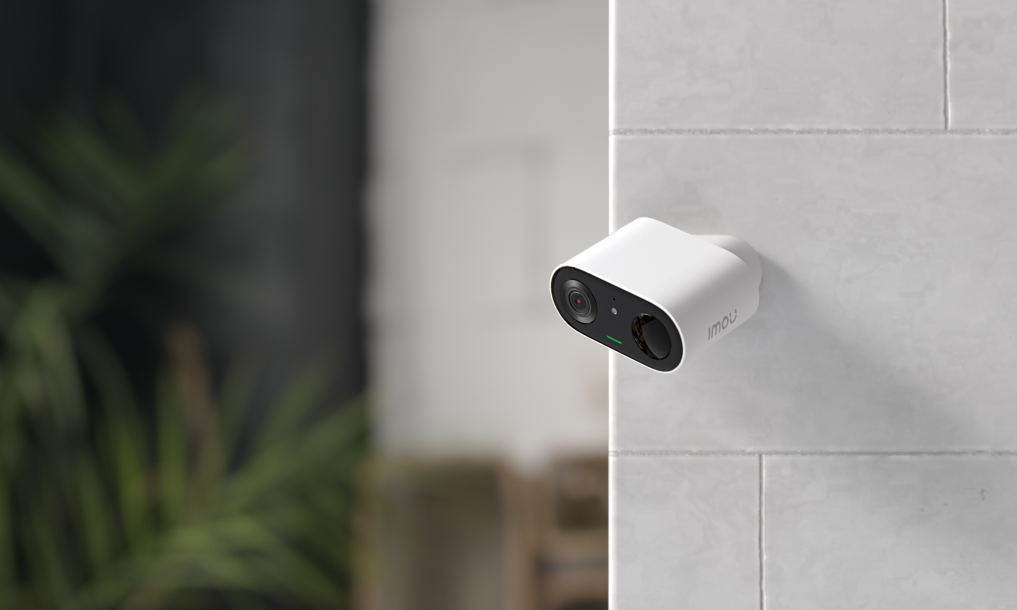 Una telecamera di sicurezza bianca è montata su un muro di piastrelle bianche. La telecamera ha un obiettivo nero ed è etichettata 'imou'.