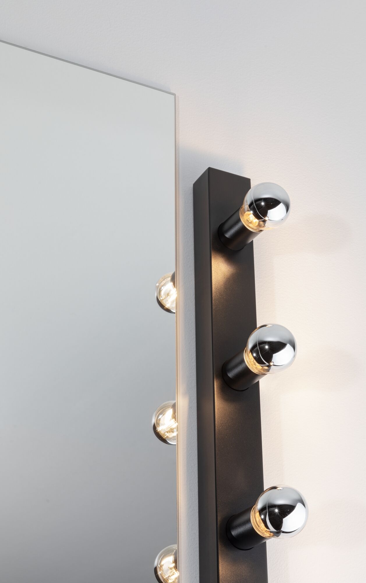 Ein Spiegel neben einer schwarzen Stange mit runden, verchromten Lichtern. Licht leuchtet von den Glühbirnen und reflektiert sich im Spiegel.