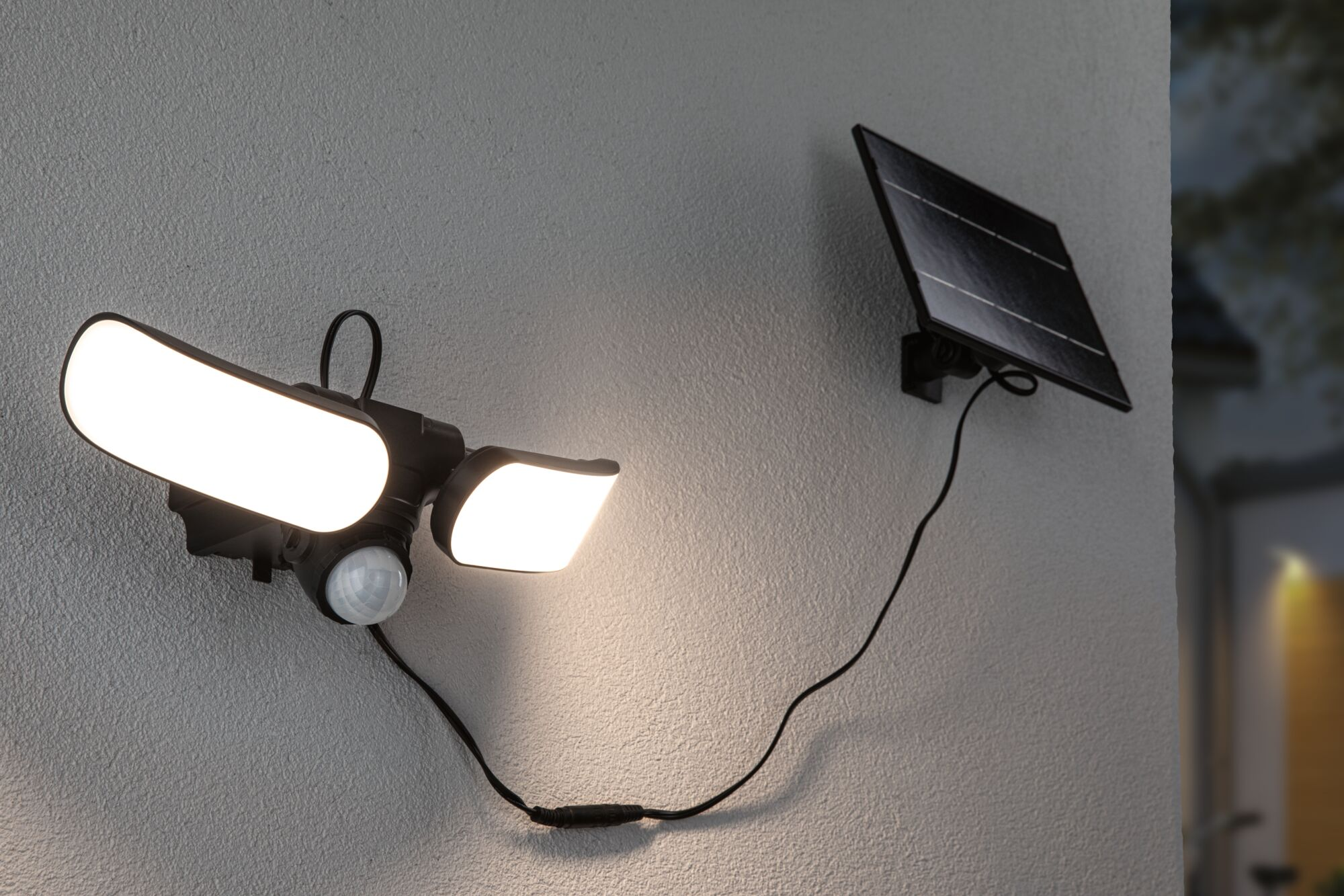 Zasilana energią słoneczną lampa bezpieczeństwa jest zamontowana na ścianie. Ma dwa jasne światła i czujnik ruchu. Podłączony jest panel słoneczny.