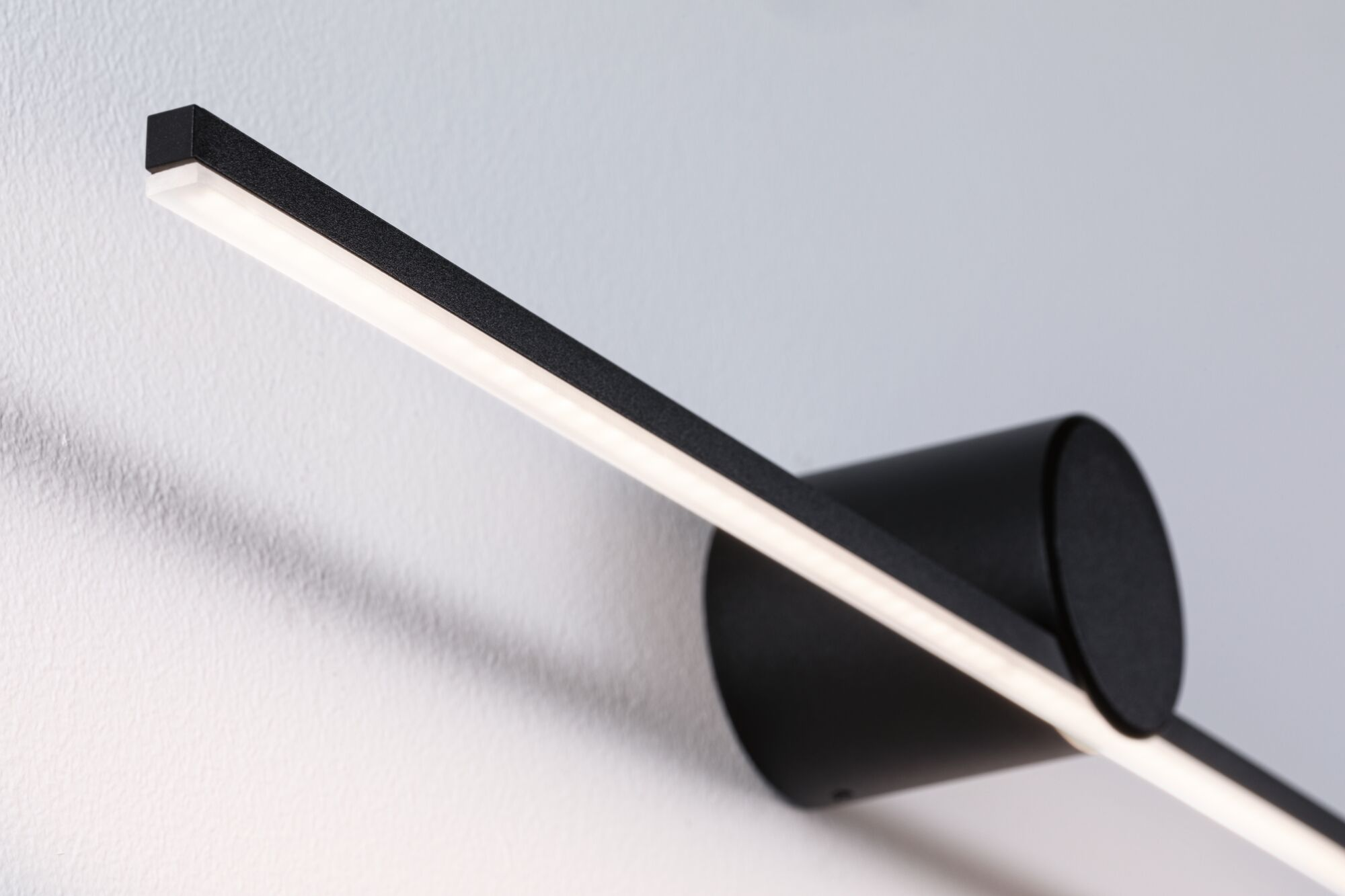 Eine moderne schwarze Wandleuchte mit hellem, linearem Licht. Sie ist an einer weißen Wand montiert.