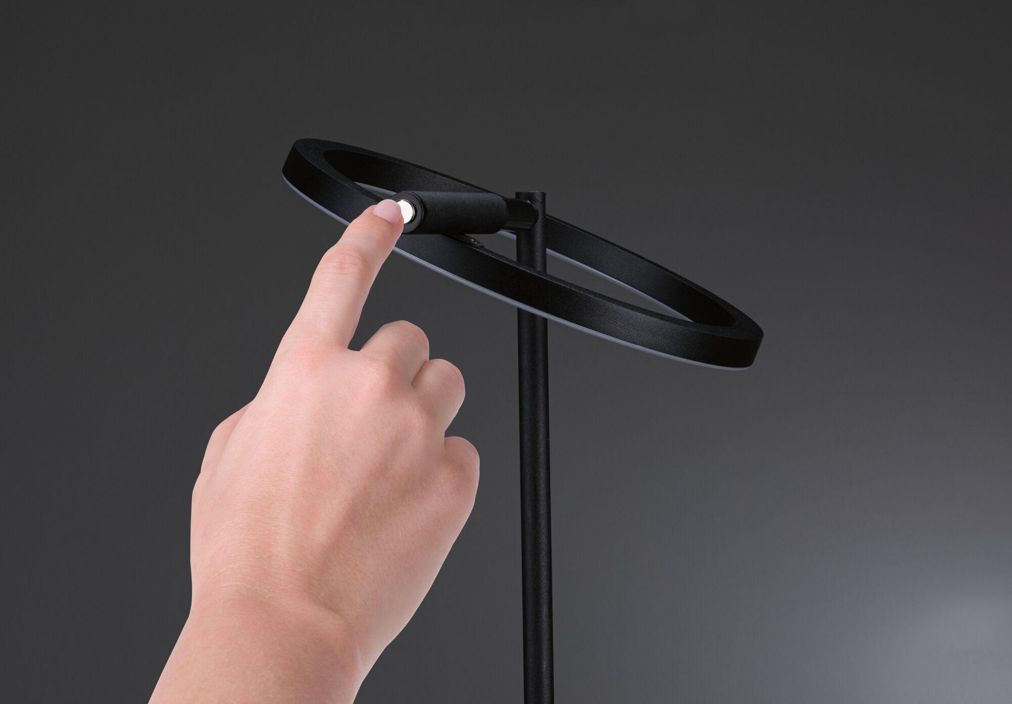 Eine Hand berührt eine schwarze kreisförmige Lampe. Die Lampe hat ein weißes Licht. Der Hintergrund ist grau.