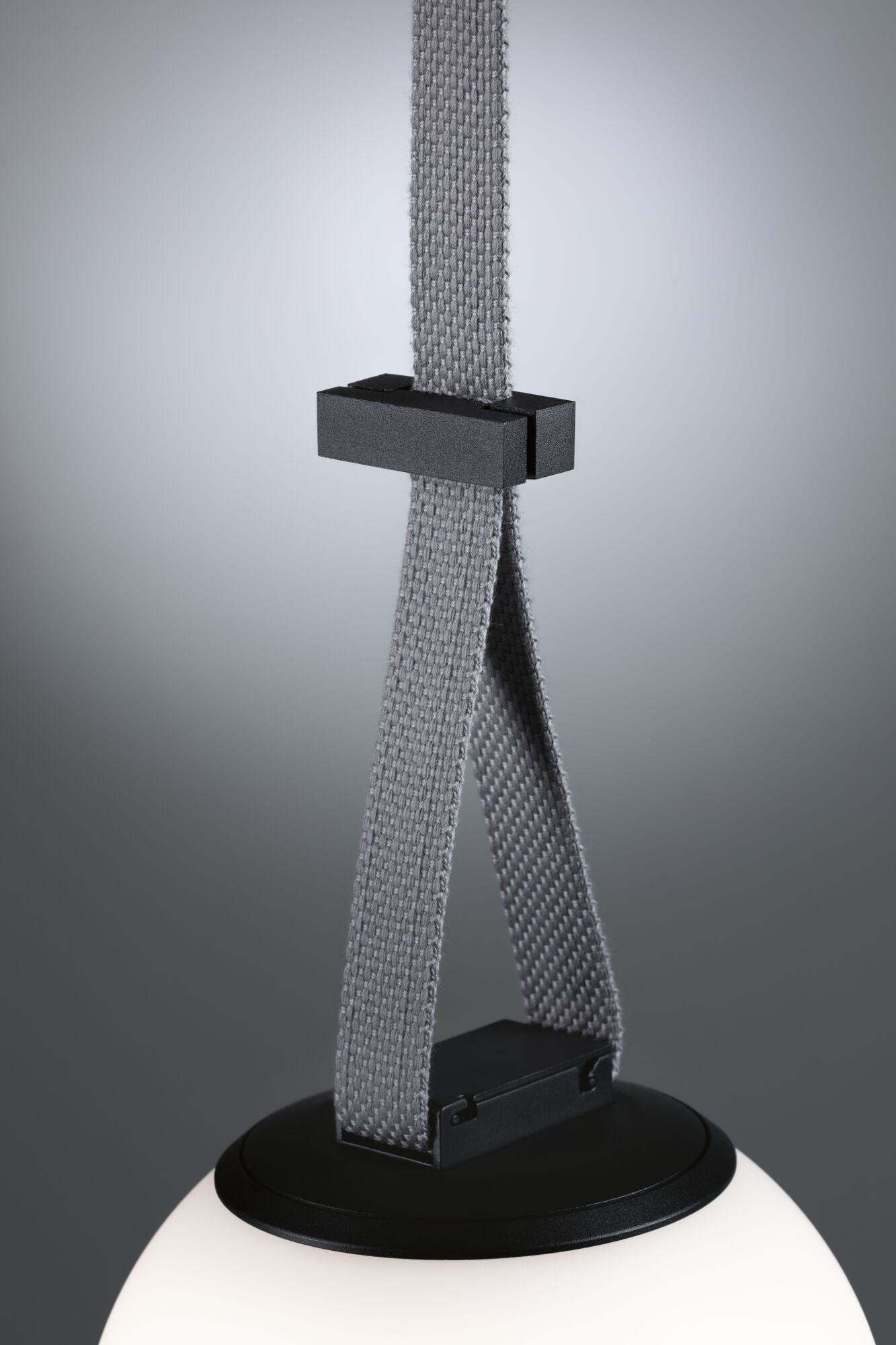 Eine moderne Lampe mit grauem Riemen und schwarzem Sockel. Das weiße Licht ist unten sichtbar. Grauer Hintergrund.
