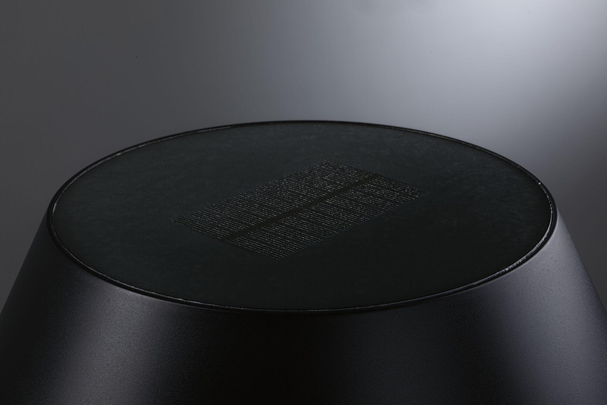 Czarny, cylindryczny obiekt z płaskim wierzchem i prostokątnym wzorem na szarym tle z gradientem.