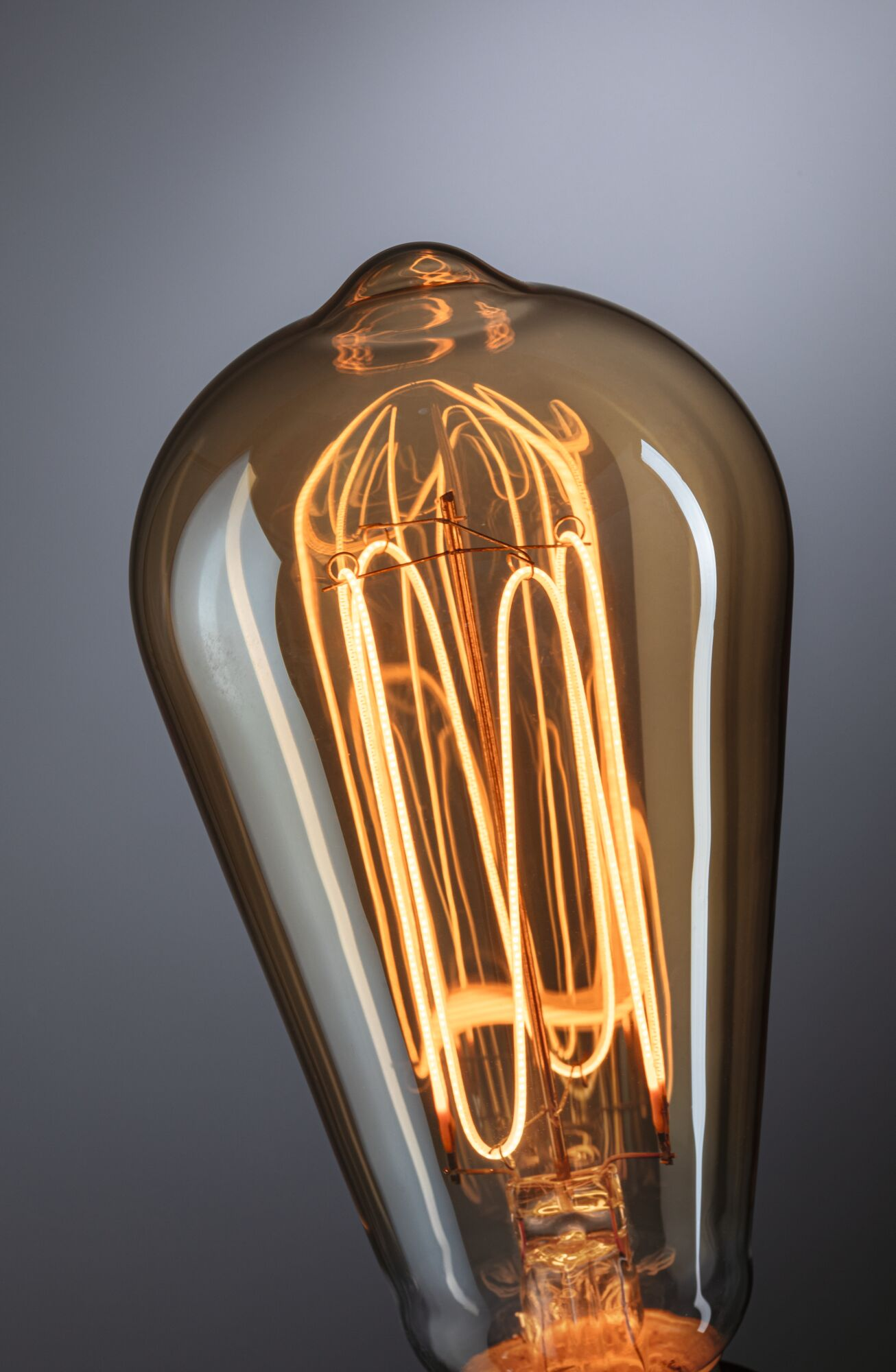 Nahaufnahme einer Vintage-Glühbirne. Das Glas ist braun, der Glühfaden leuchtet orange. Der Hintergrund ist ein grauer Farbverlauf.