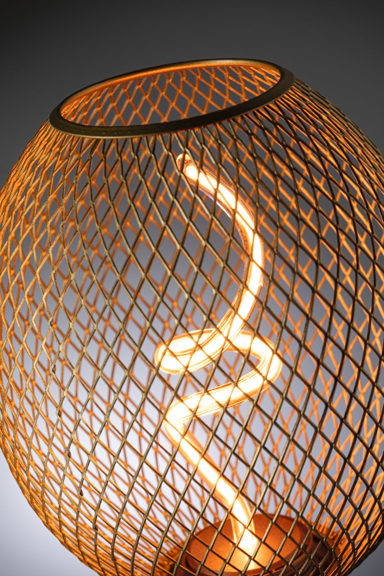 Złota metalowa lampa w klatce ze świecącą żarówką spiralną w środku, na szarym tle gradientowym.