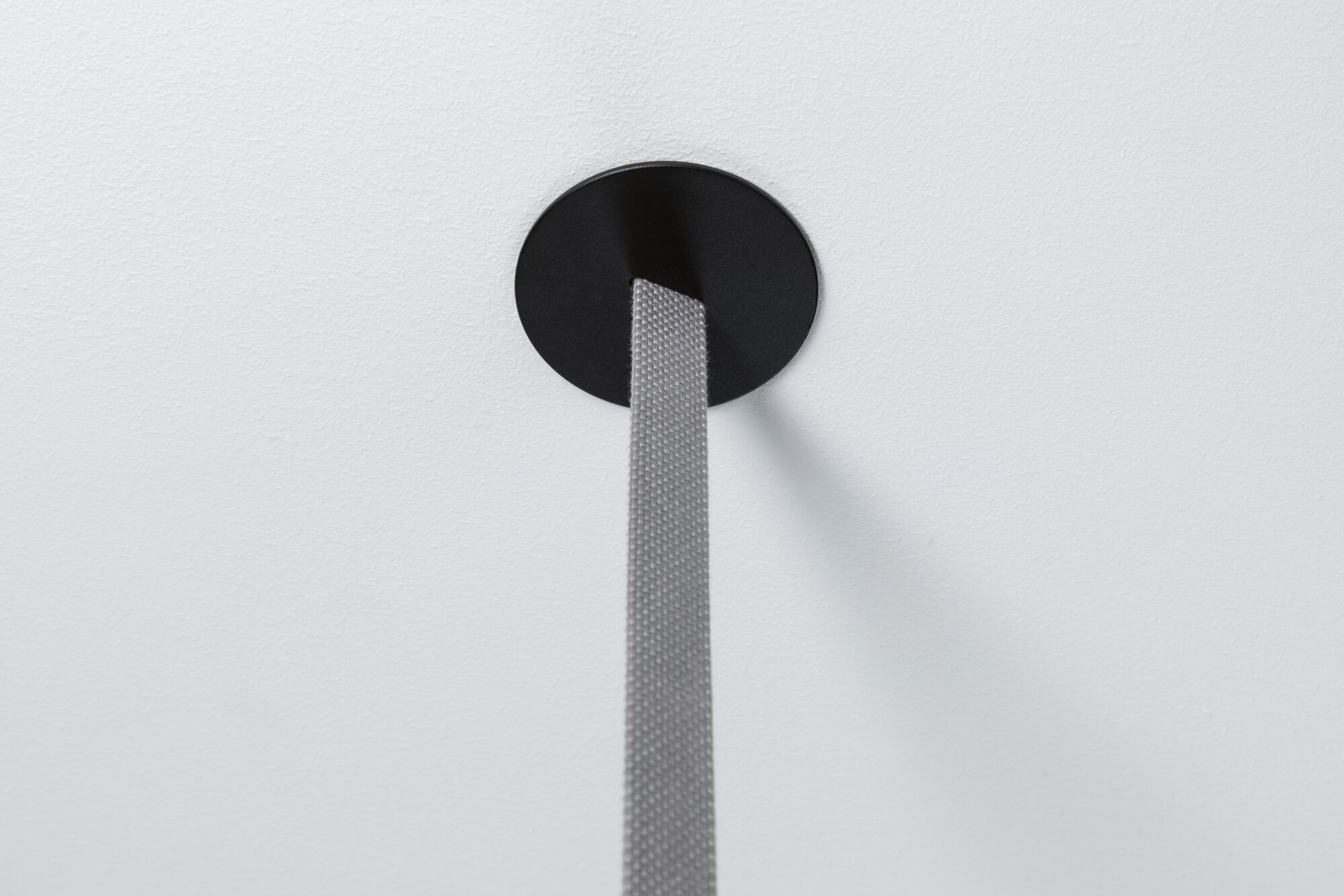 Szary pasek wychodzi z czarnego koła na białej ścianie. Pasek jest wyśrodkowany, a cień pada w prawo.