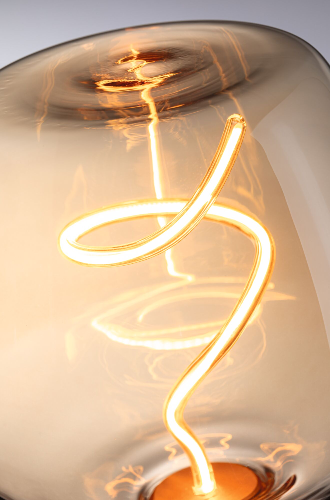 Zbliżenie żarówki w ciepłym odcieniu. Żarzący się, spiralny żarnik znajduje się w szklanej żarówce. Żarówka odbija światło.