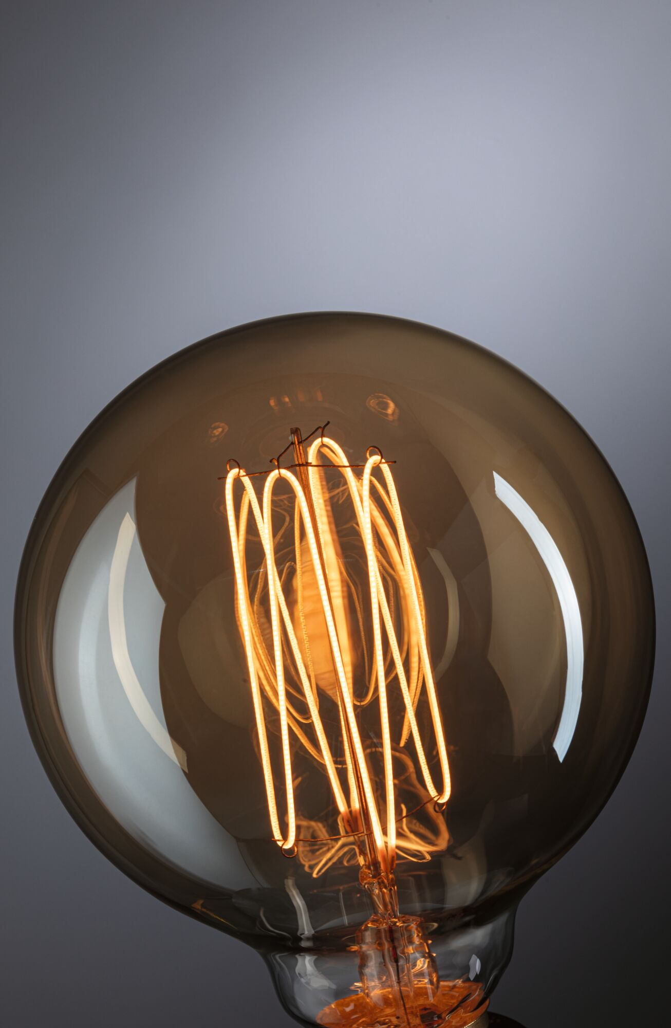 Nahaufnahme einer Glühbirne im Vintage-Stil. Das Glas ist braun getönt, der Glühfaden leuchtet orange. Der Hintergrund ist grau.