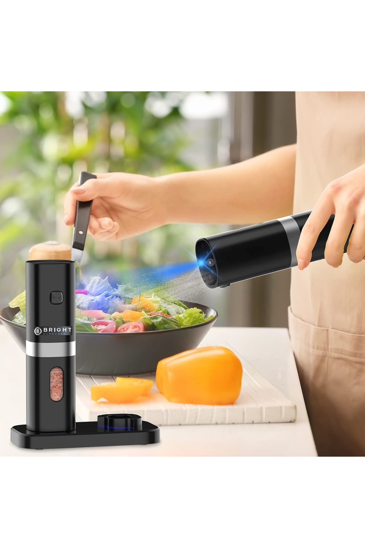 Bir kişi siyah bir cihazla salataya püskürtme yapıyor. İkinci bir cihaz salatanın yanında duruyor. Malzemeler ve bir biber görülebilir.
