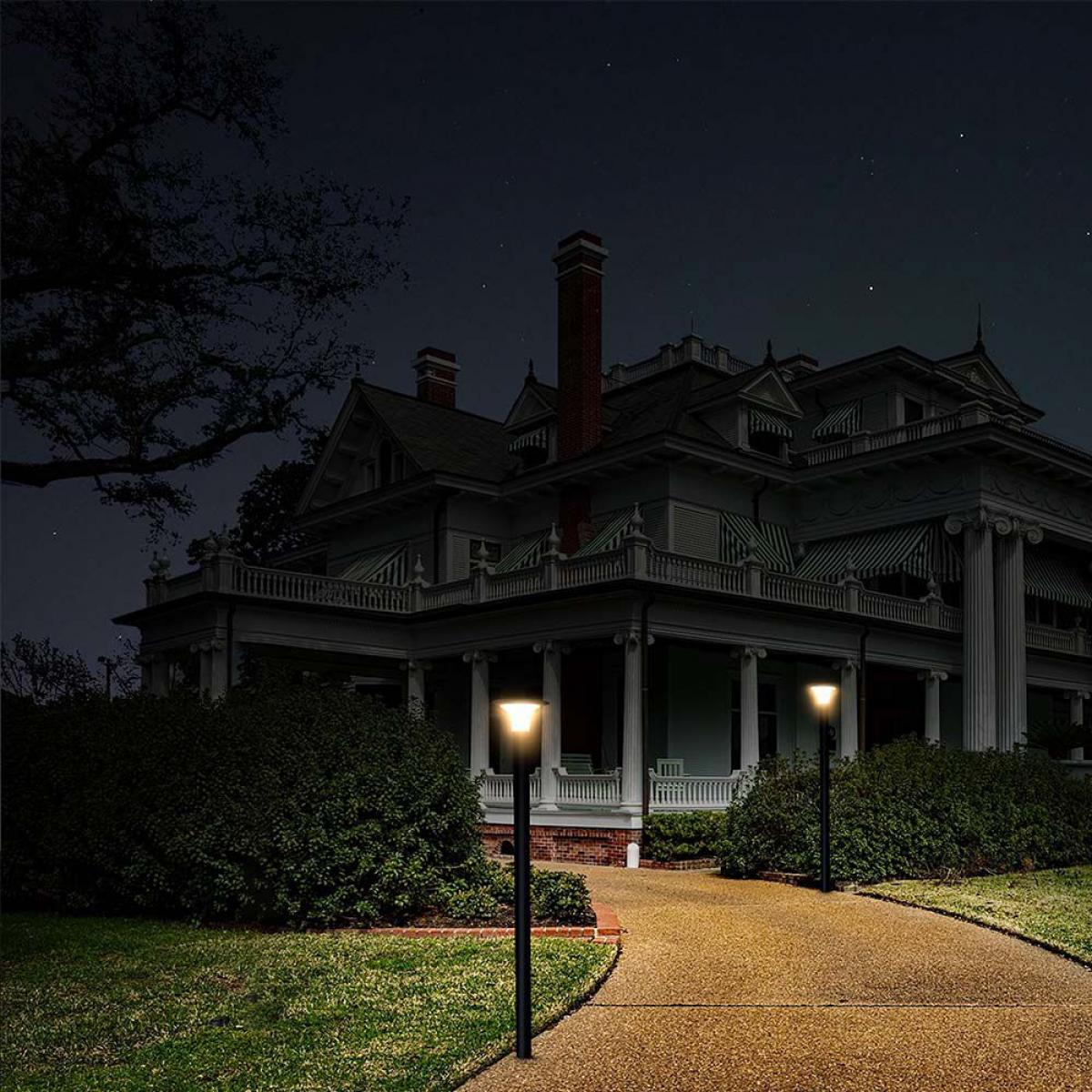 Eine Villa bei Nacht mit beleuchteten Lampen auf einem Weg. Büsche und Gras im Vordergrund, Sterne am Himmel.