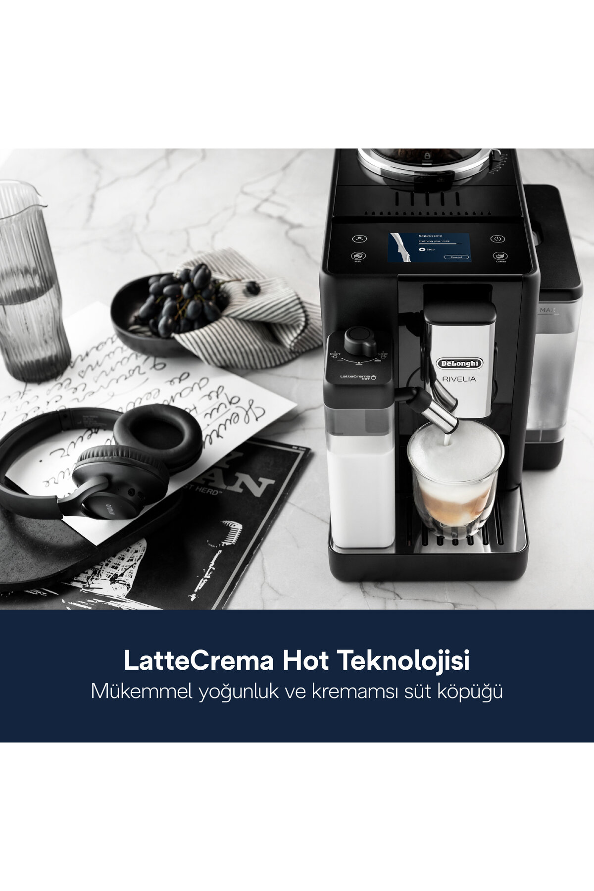 Una macchina da caffè nera con un bicchiere di latte macchiato. Uva, cuffie e un bicchiere sono sul tavolo.